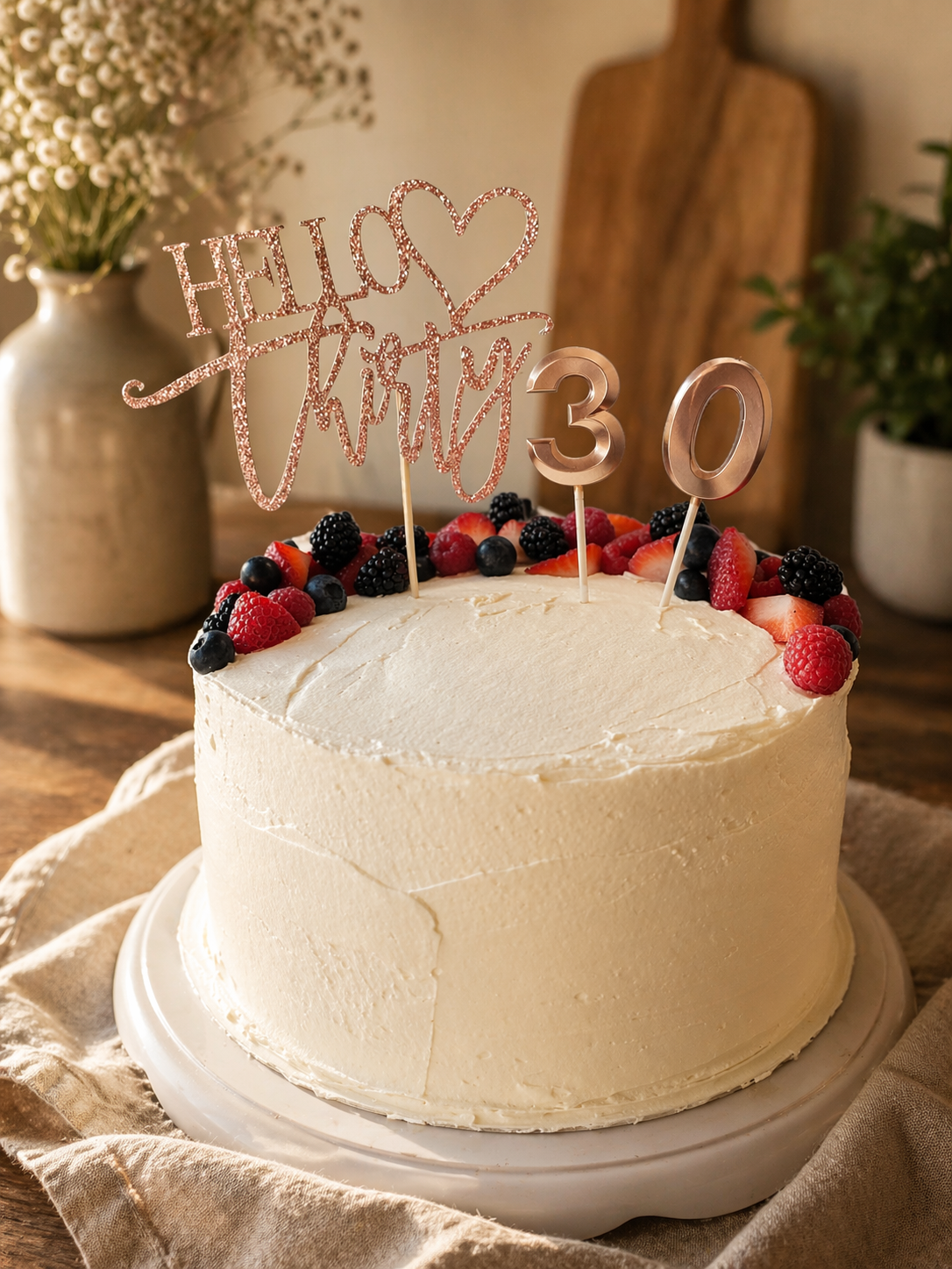 A white frosted birthday cake decorated with mixed berries, topped with a