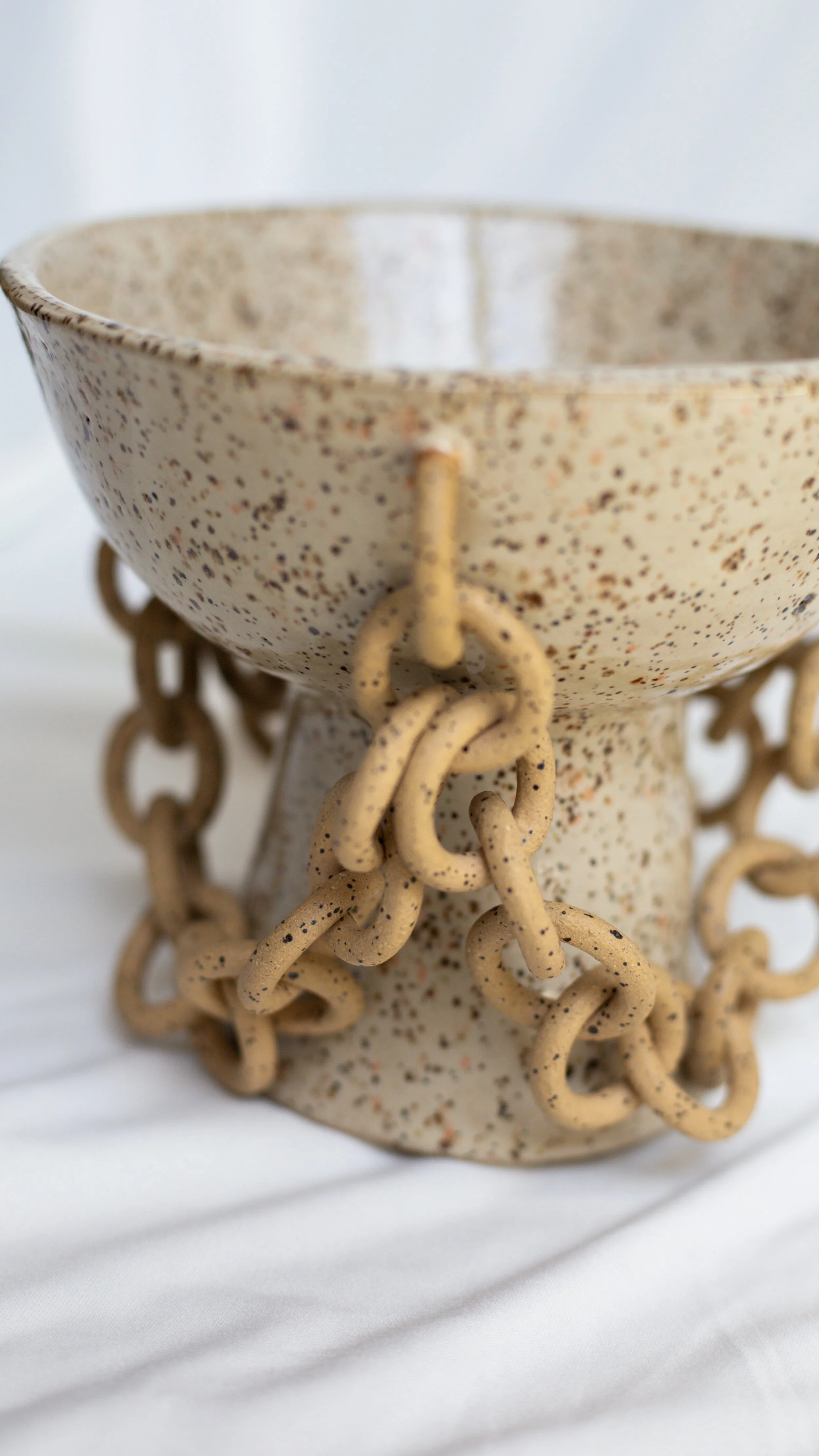 A speckled ceramic bowl with attached chains around its base.