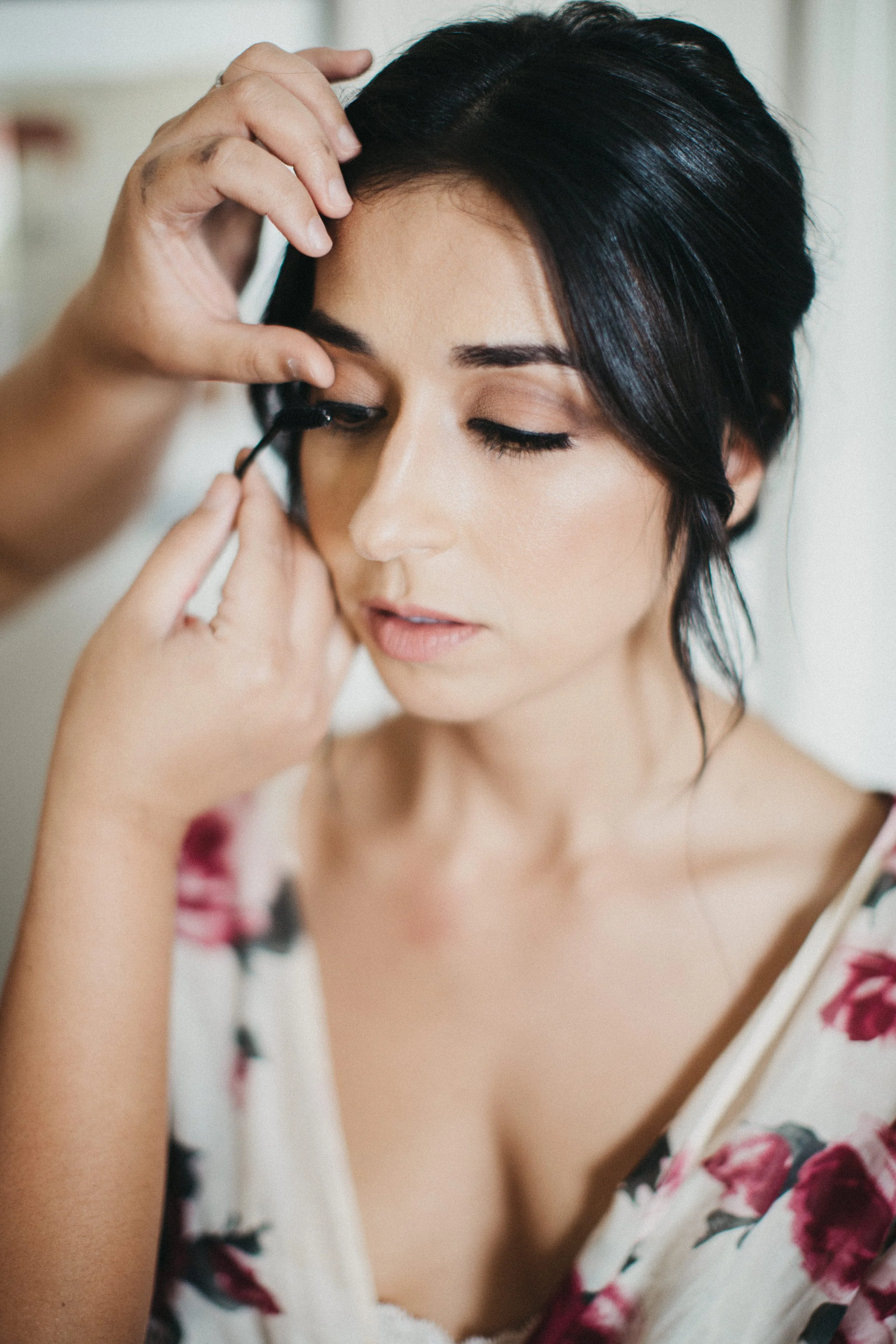A woman with short black hair getting her makeup done, having eyeliner applied by a makeup artist
