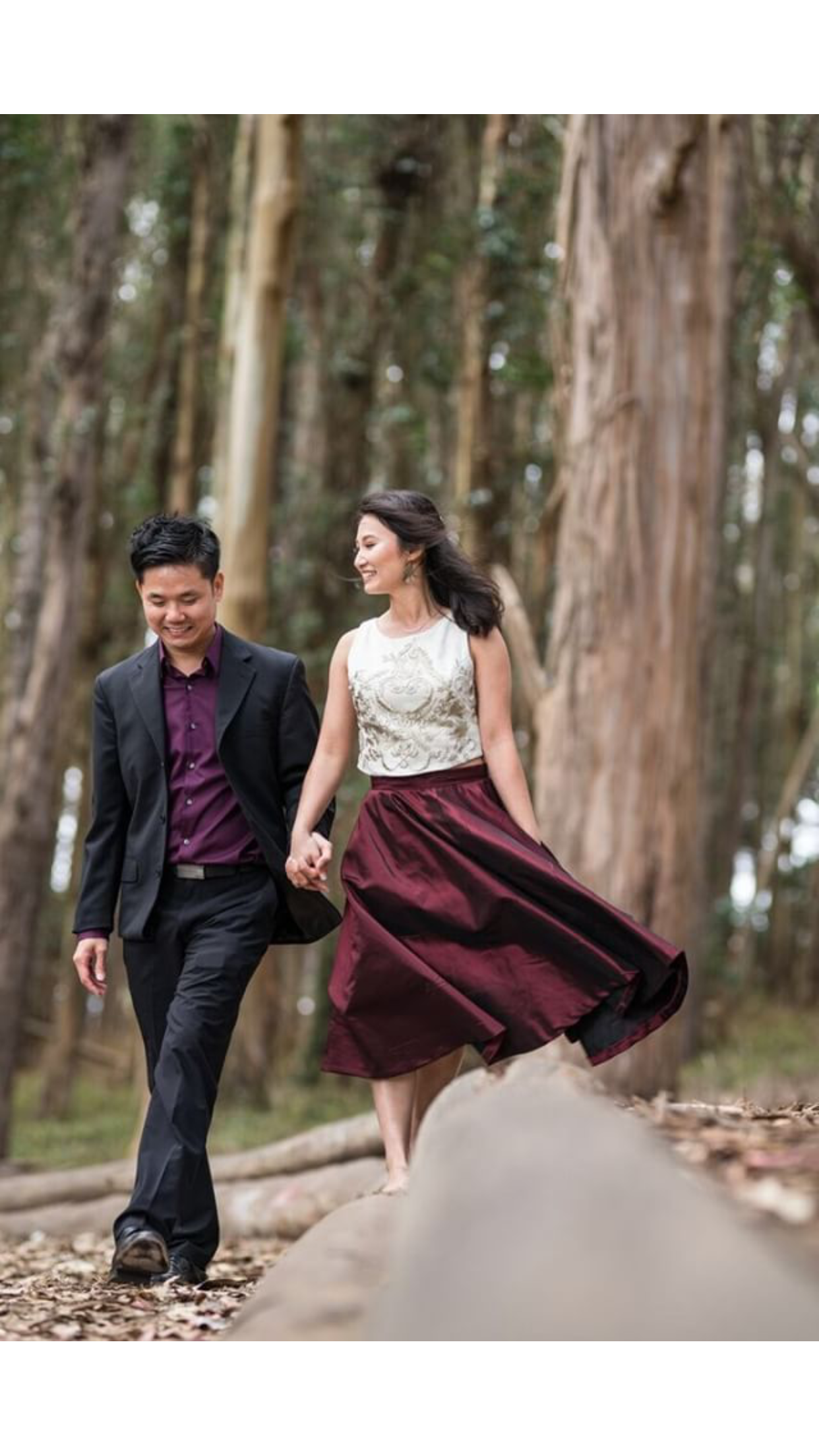 A happily walking couple in forest, holding hands, dressed in semi-formal attire, smiling and enjoying nature.