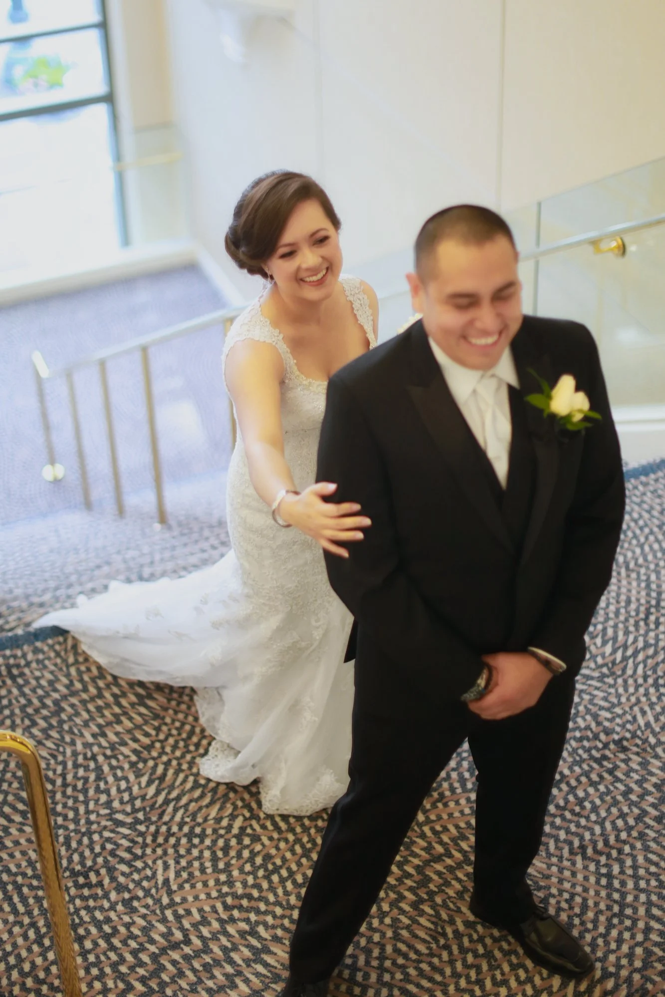 A bride and groom standing on a staircase, with the bride smiling and playfully tugging at the groom's tuxedo.