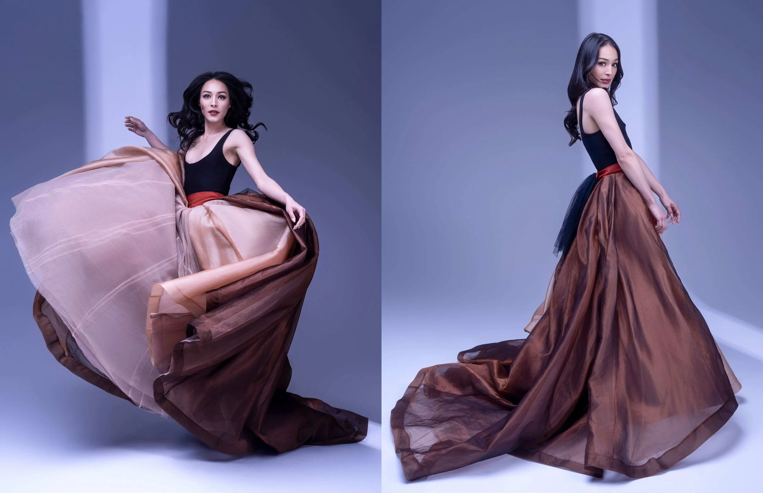 A woman with long dark hair wearing a black top and a flowing brown and orange skirt, posing against a studio background.