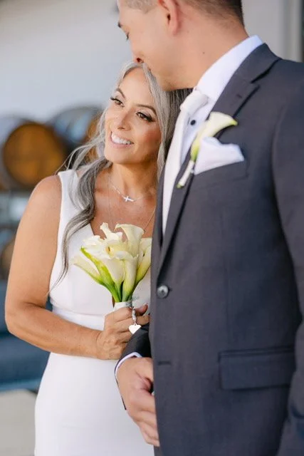 A bride holding a bouquet of white calla lilies, smiling at her groom during their wedding ceremony.