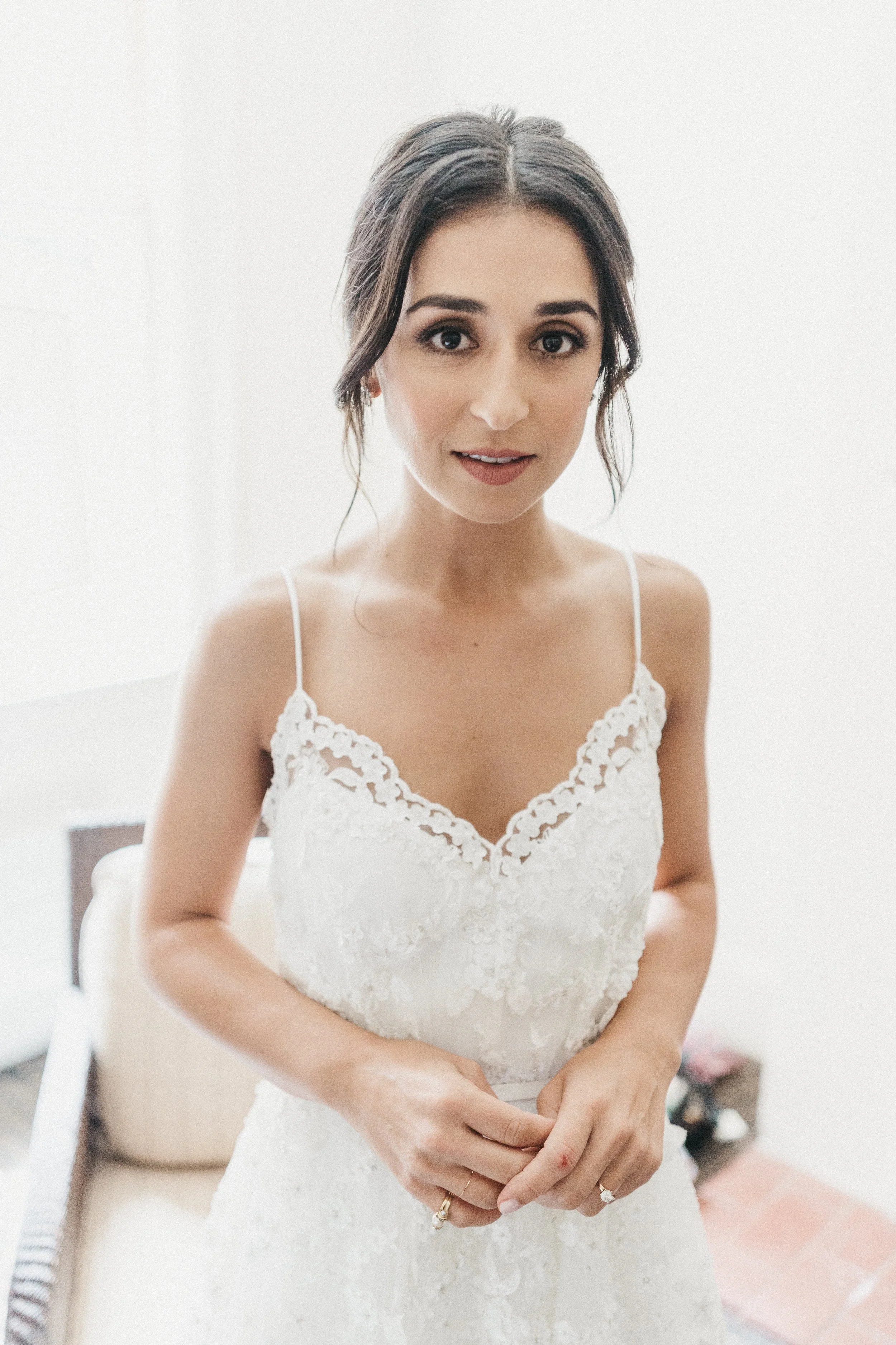 A woman in a white lace dress standing indoors, looking at the camera.