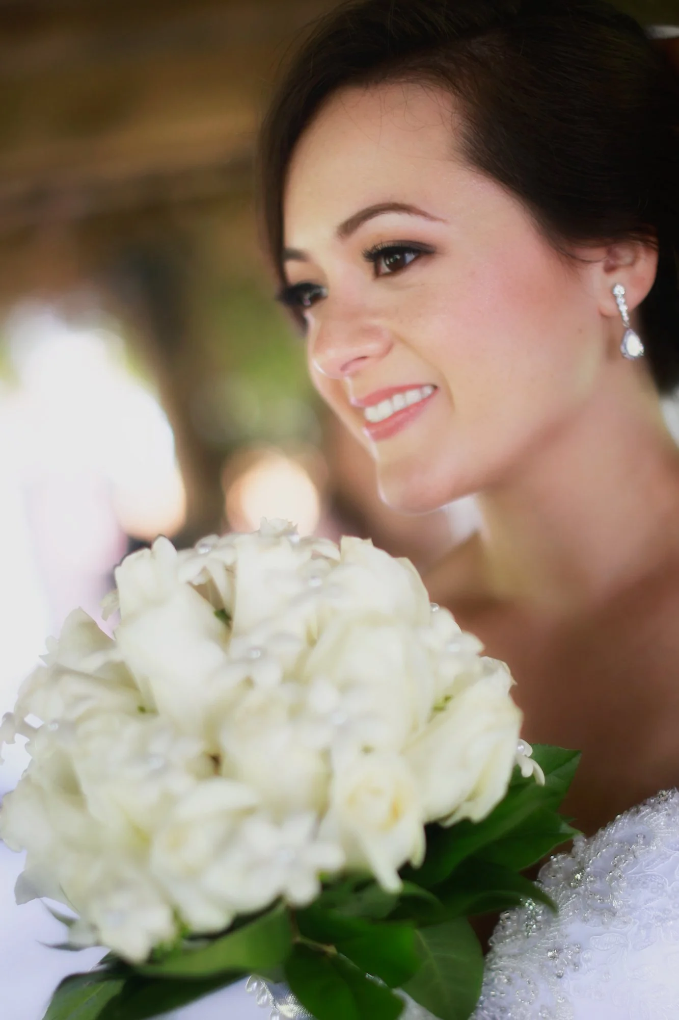 A bride with dark hair and earrings holding a white bouquet, smiling.