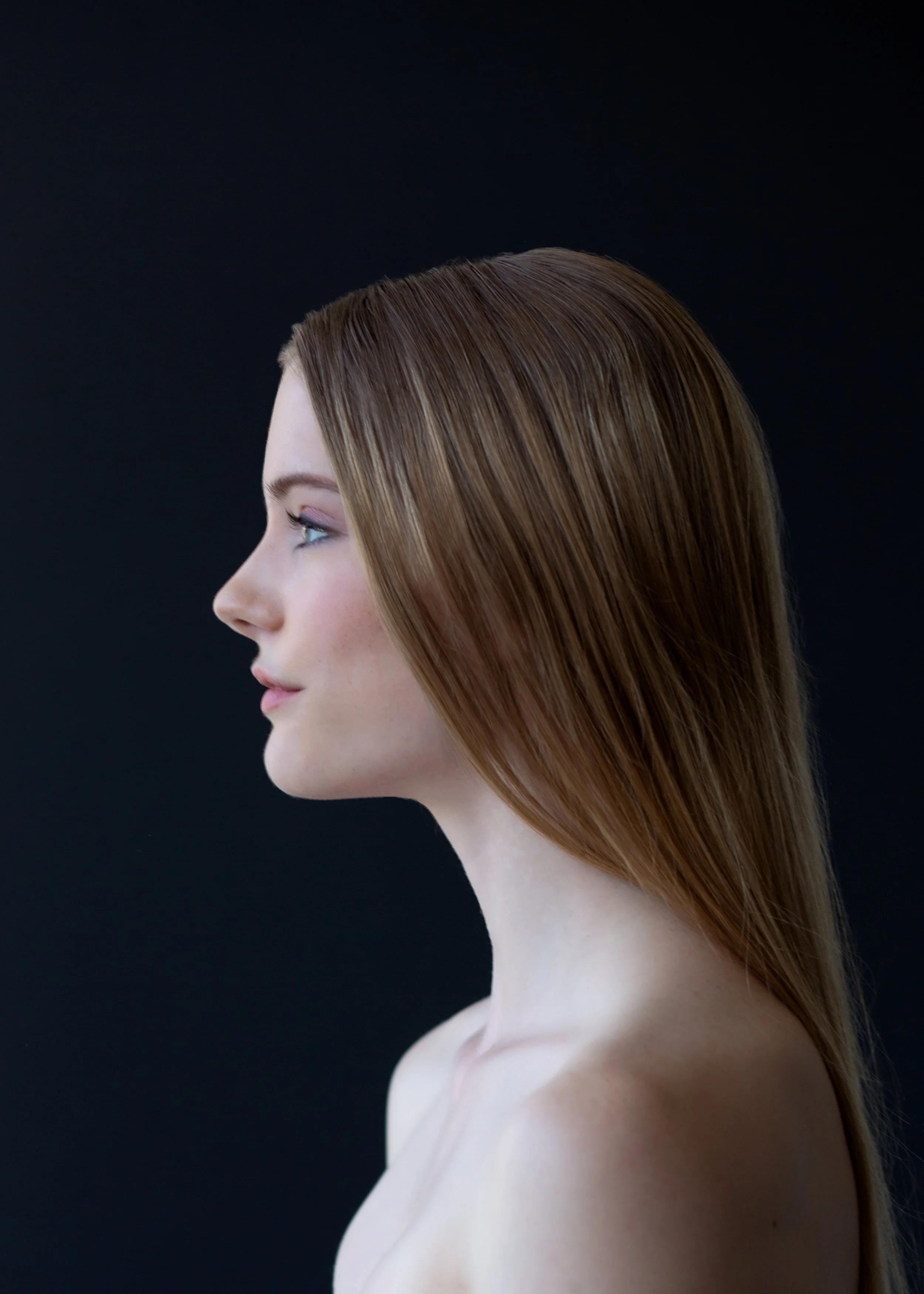 Profile of a young woman with straight, reddish-brown hair and fair skin against a dark background