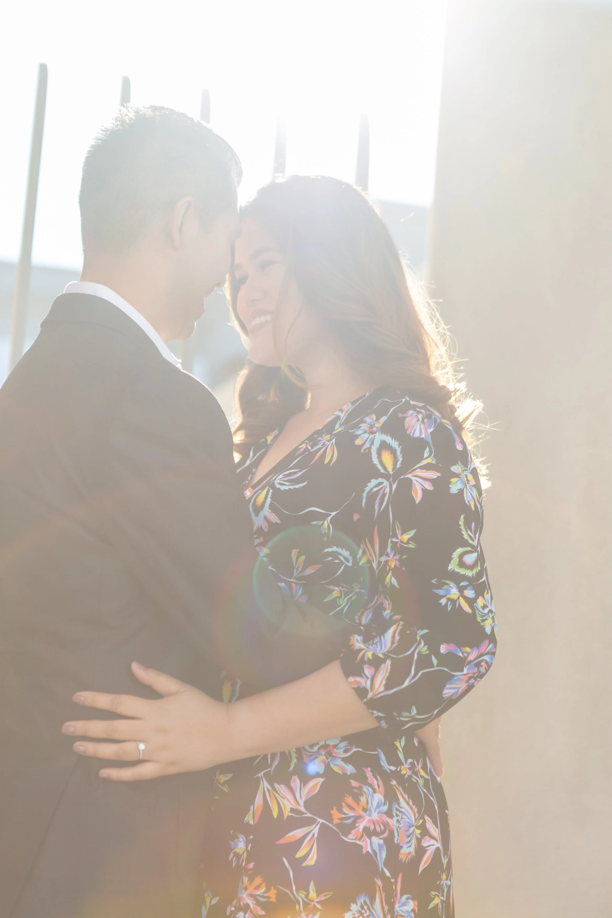 A couple intertwining during a tender moment with sunlight shining behind them.