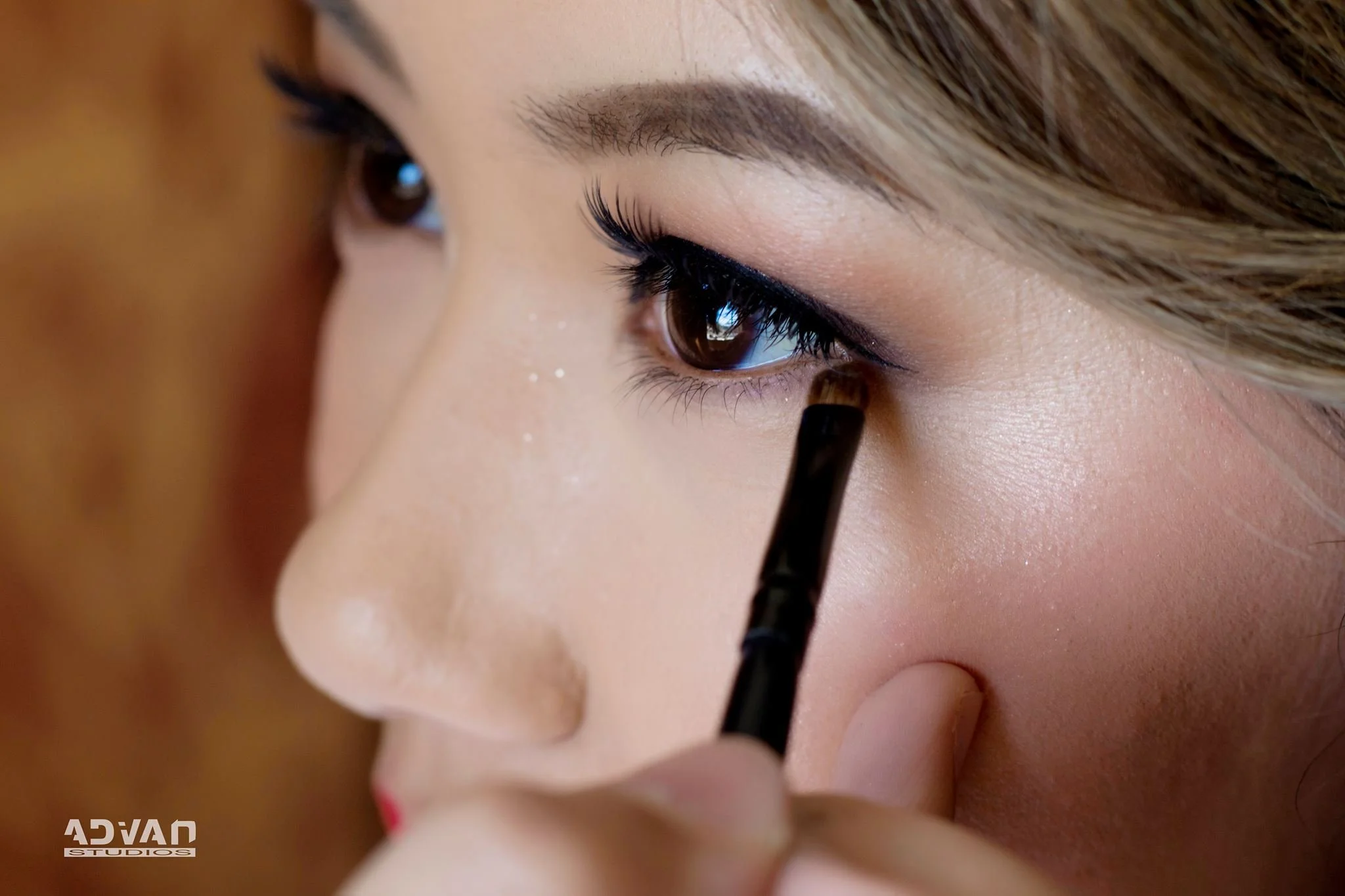 Close-up of a woman's face with makeup, as she applies eyeliner with a small brush.