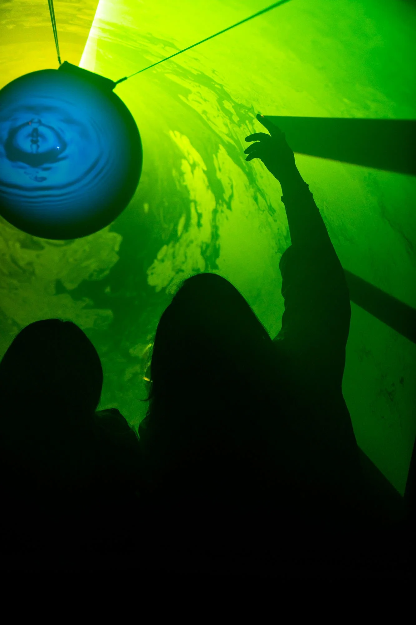 Silhouette of a person with an arm extending towards a large, glowing green sphere or object, with a green and yellow textured background.
