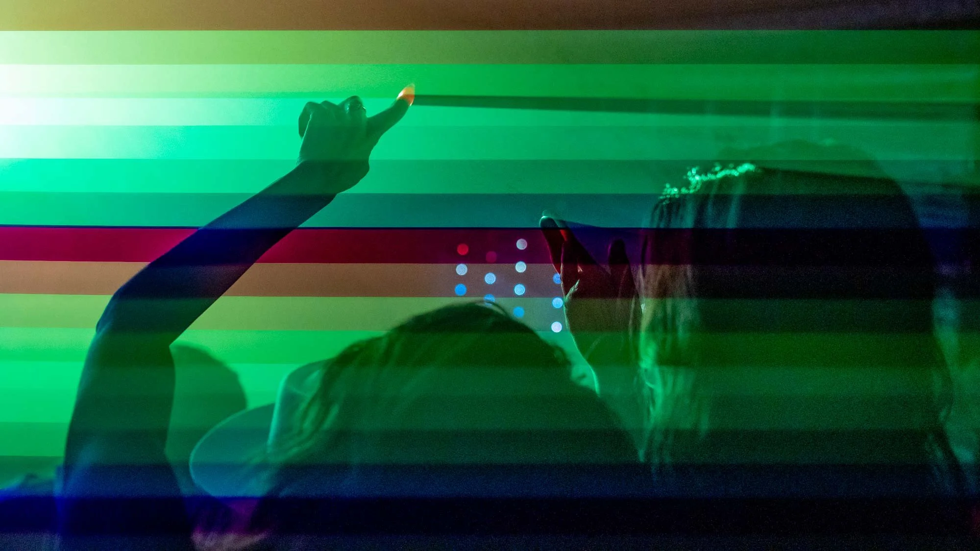 A person with long hair and another with raised hands silhouetted against a backdrop of colorful, horizontal light streaks and dots.