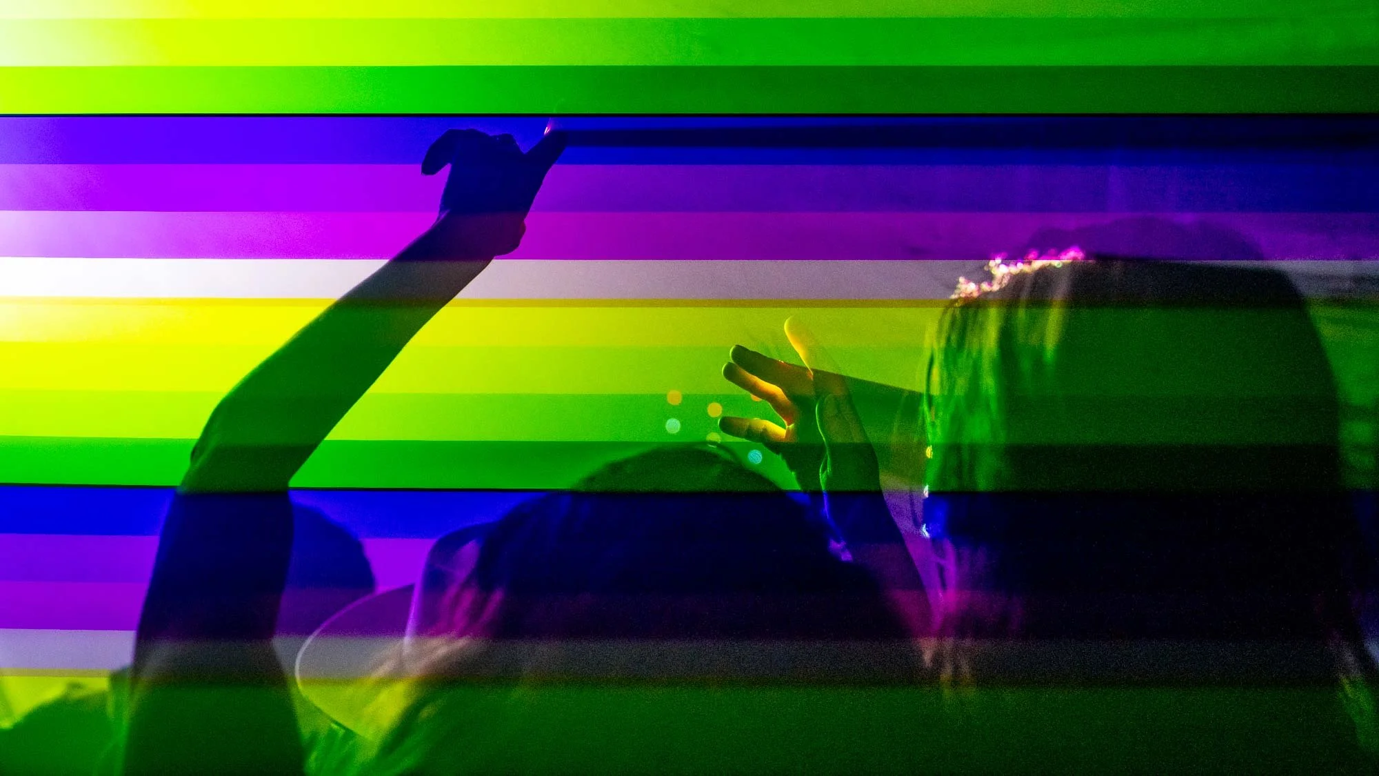 Silhouettes of two people interacting with a colorful, striped digital display or screen with vibrant, rainbow-like colors.