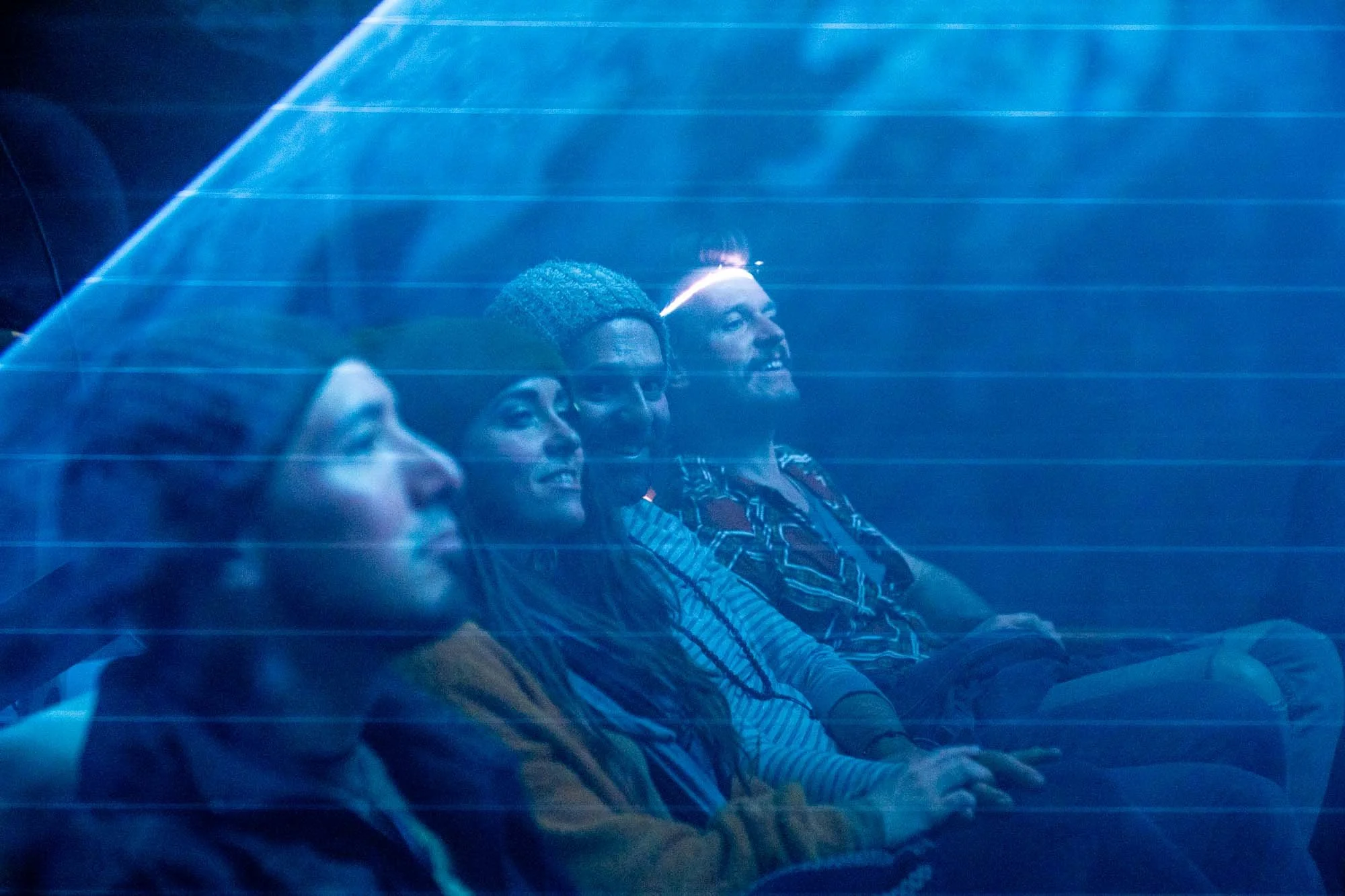 Four people sitting in a row, illuminated by blue light, enjoying a concert or event, smiling and laughing.