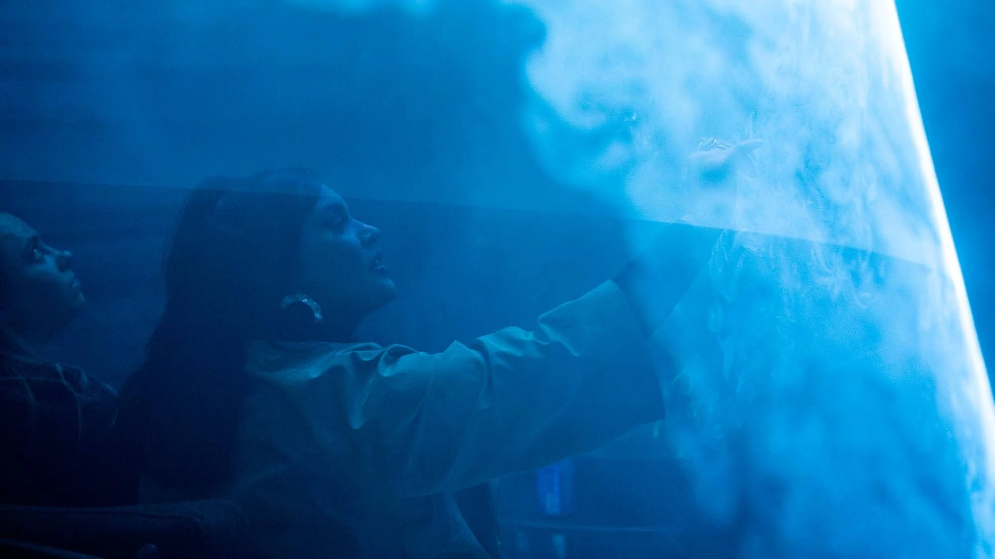 People observing an ice sculpture or ice wall, looking at it with interest in a cool, blue-toned environment.