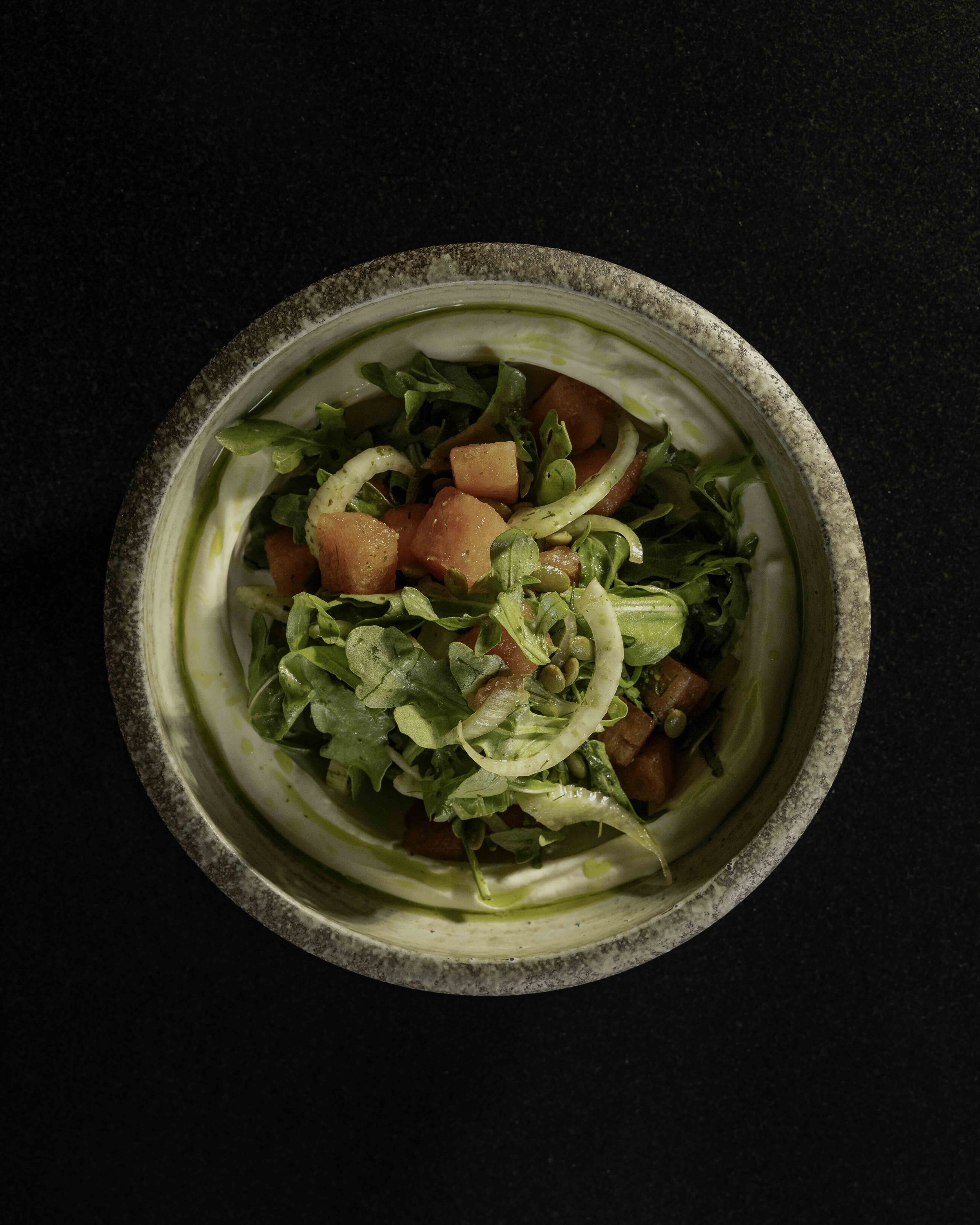 A top-down view of a bowl of salad containing leafy greens, diced tomatoes, and sliced onions on a dark surface.