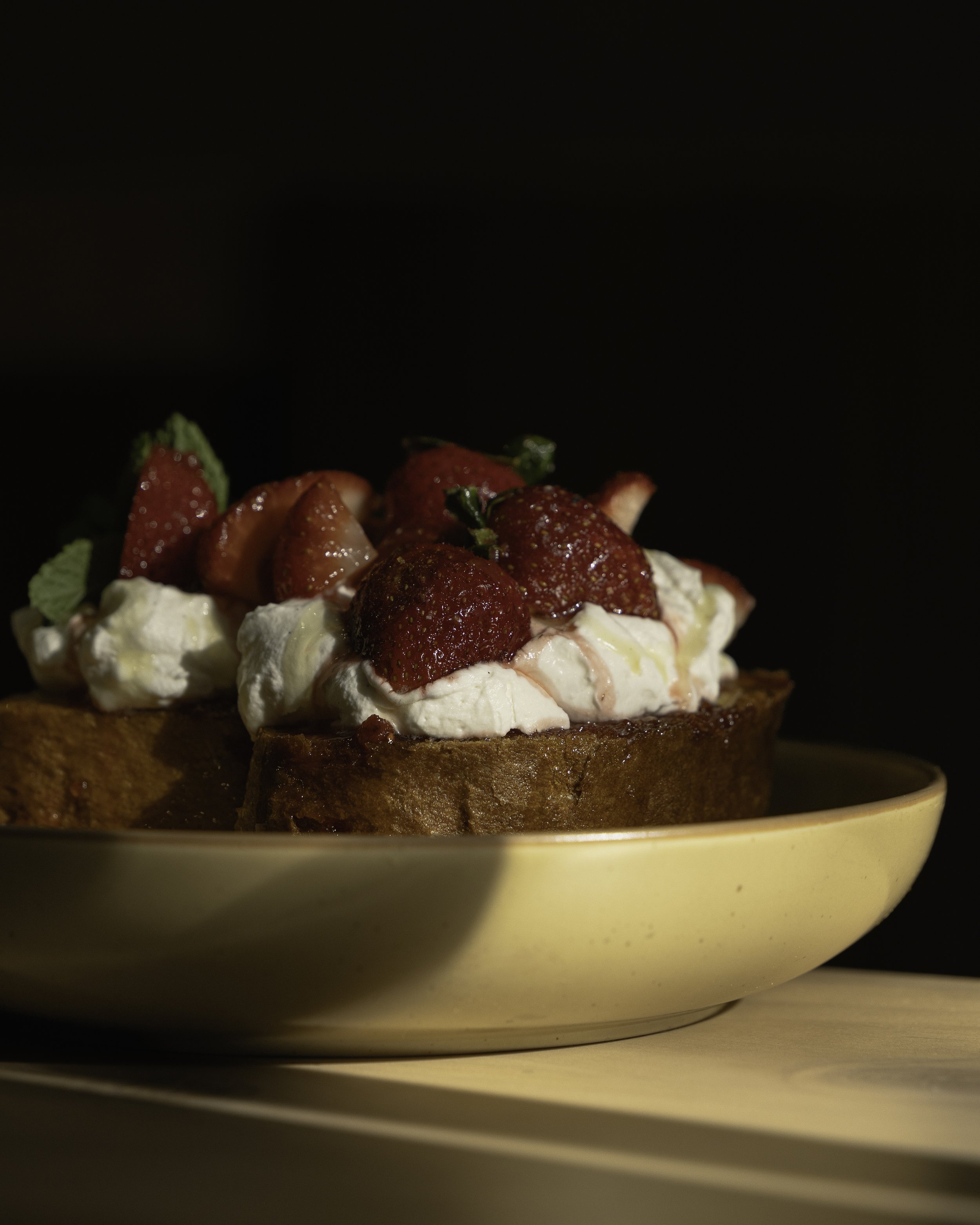 Close-up of a slice of French toast topped with whipped cream and fresh strawberries on a yellow plate.