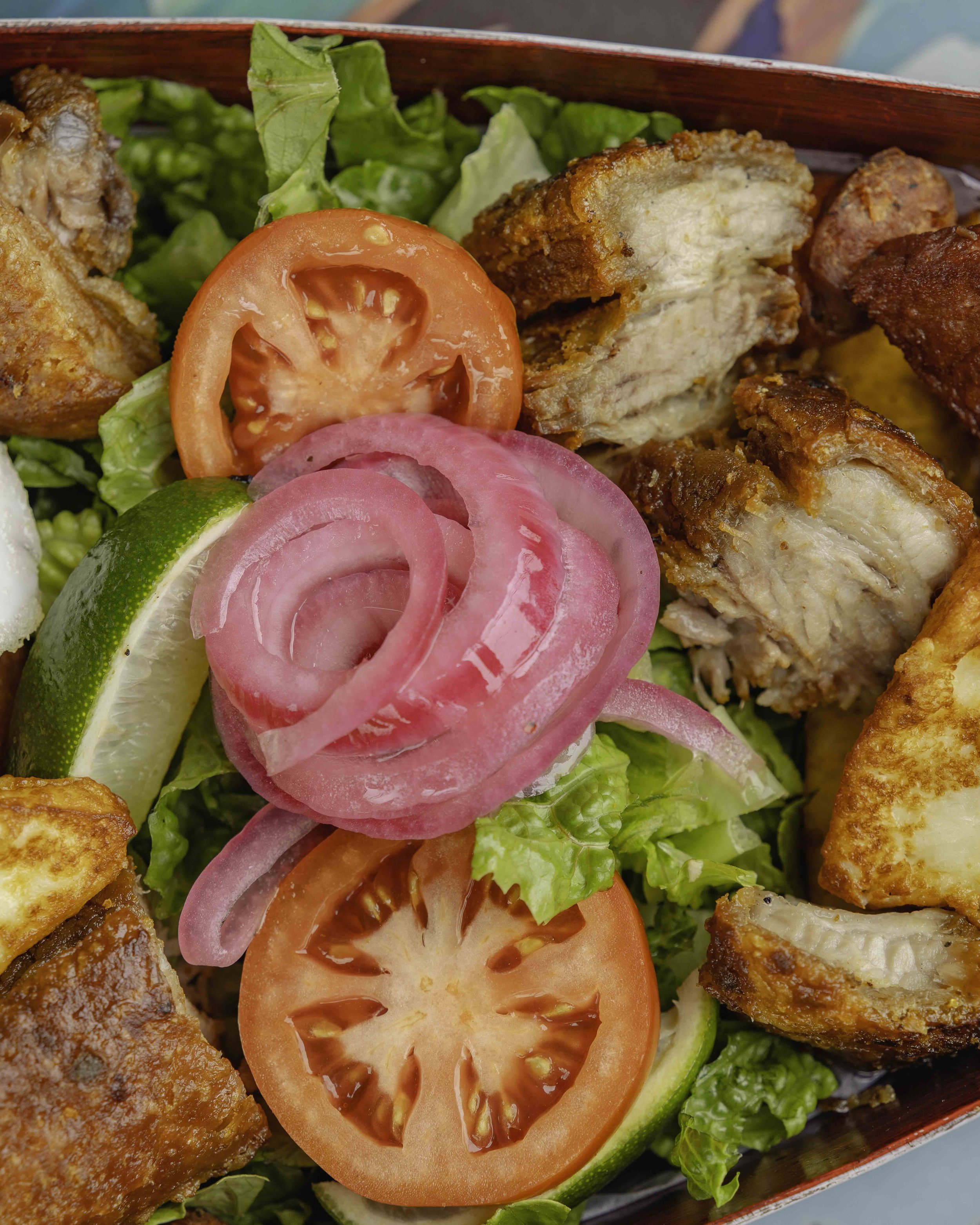 Close-up of a fresh salad with sliced tomato, red onion, lime, lettuce, and fried chicken pieces.