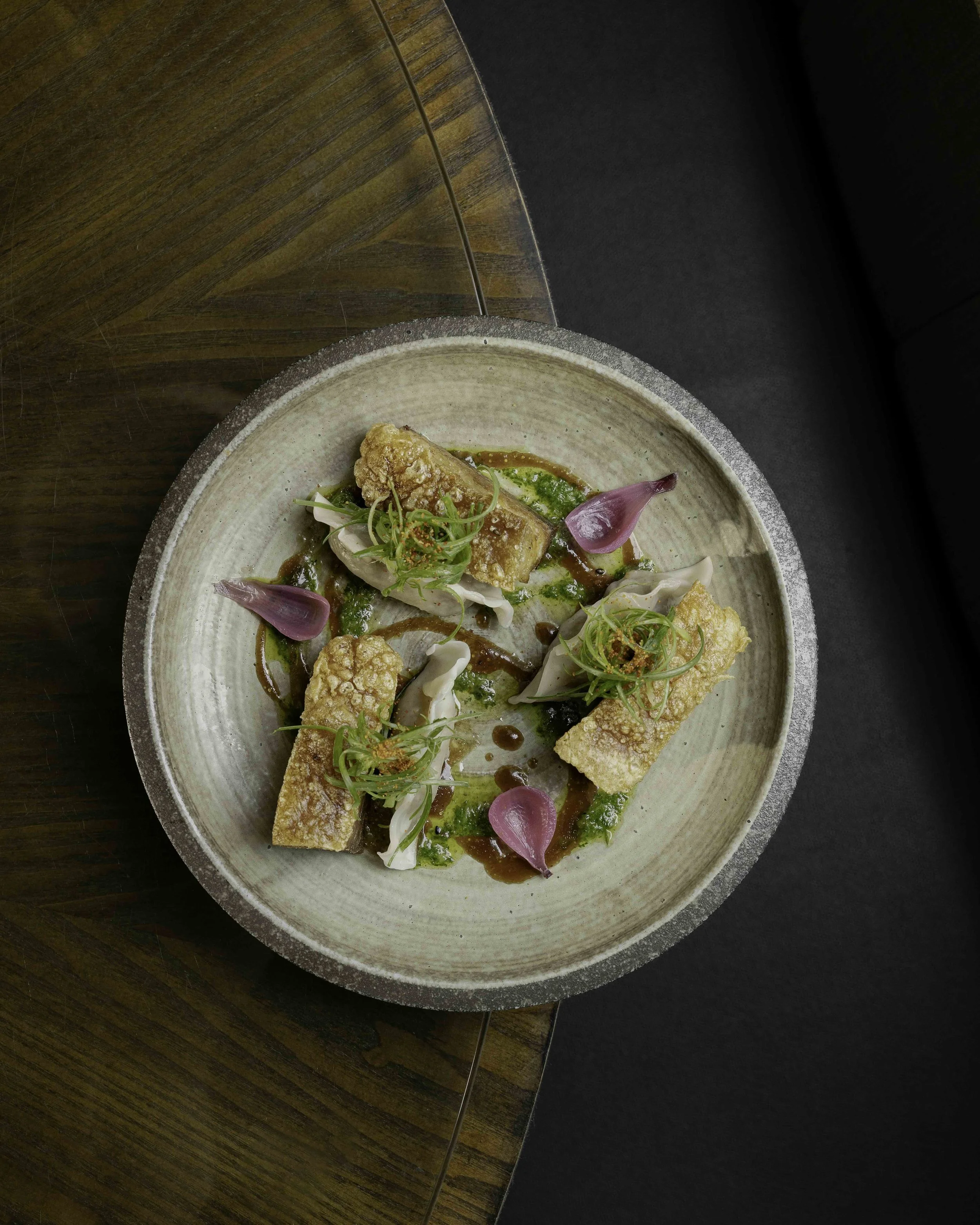 Plate with fried fish fillets, garnished with microgreens, edible flowers, and sauce, on a ceramic dish.