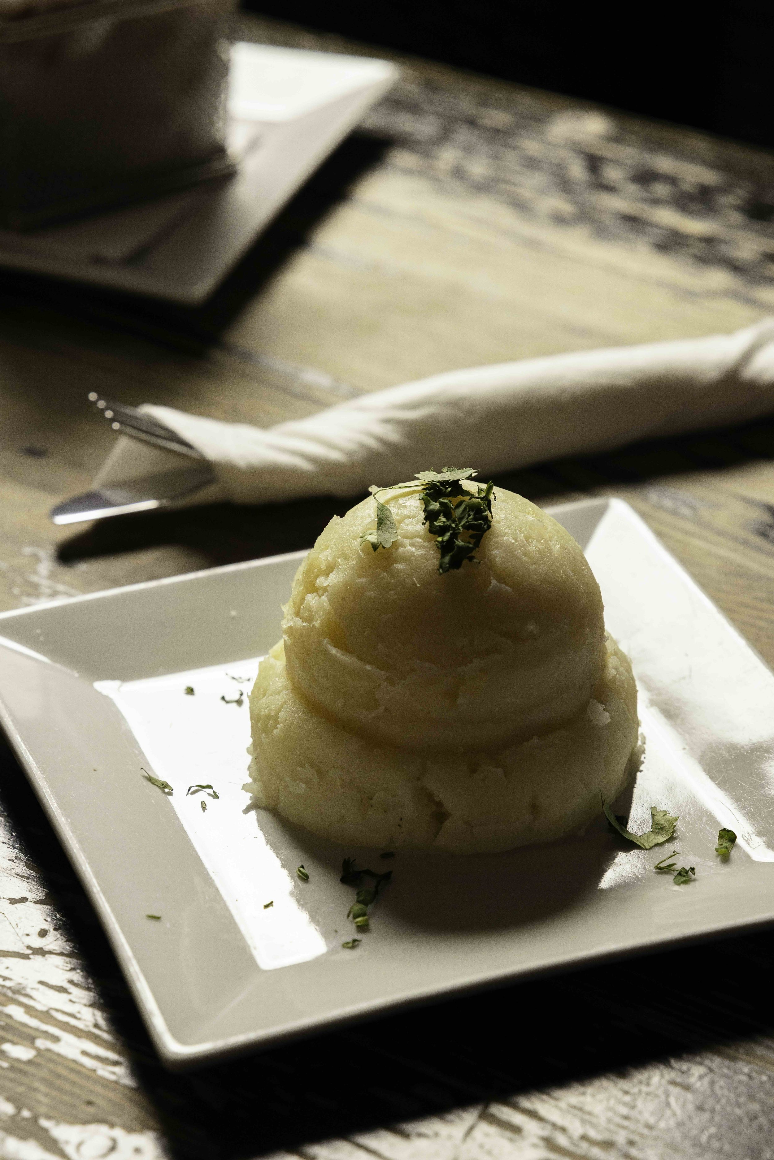 A scoop of mashed potatoes garnished with chopped herbs on a white square plate.