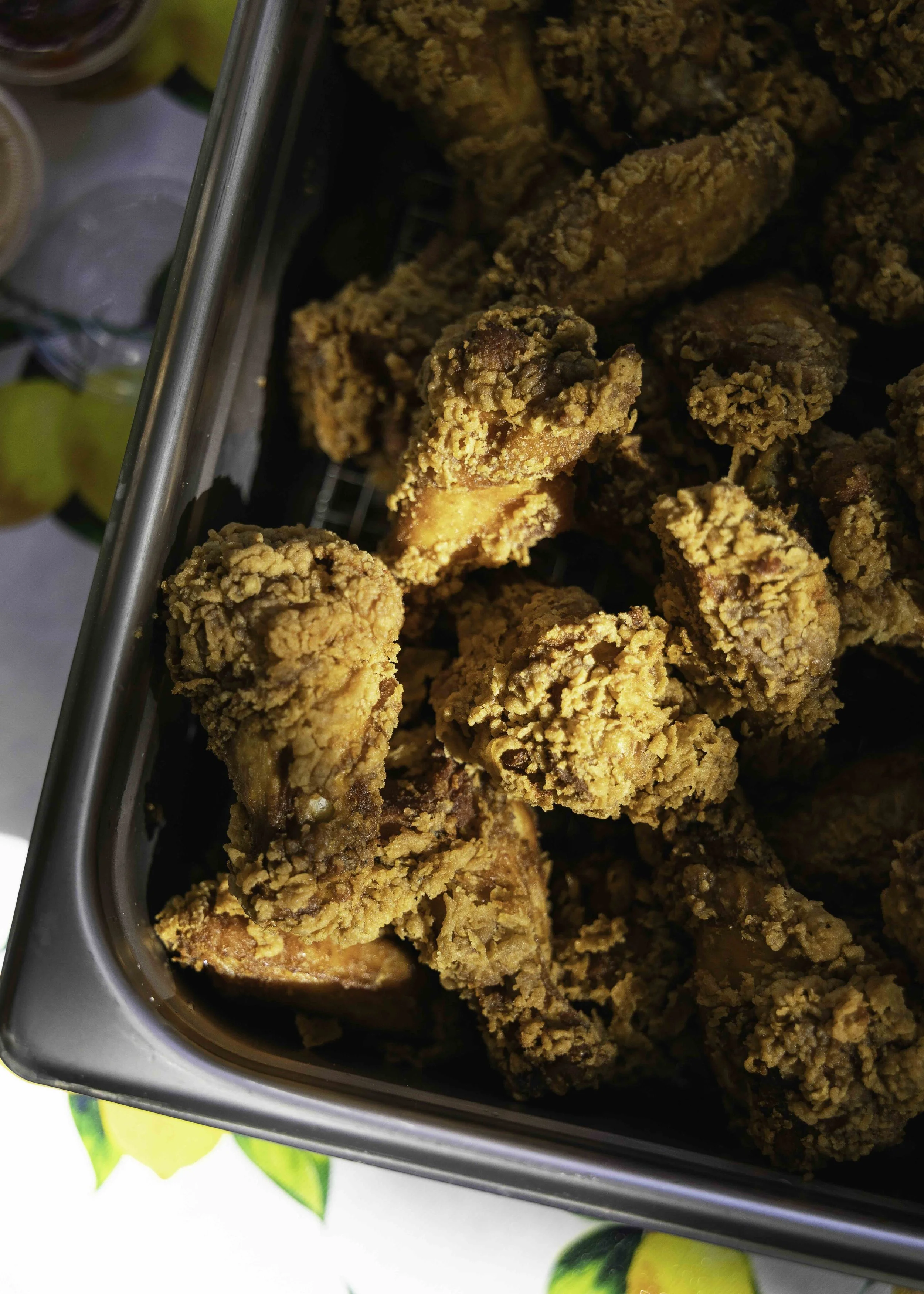Fried chicken drumsticks and pieces in a stainless steel container on a table.