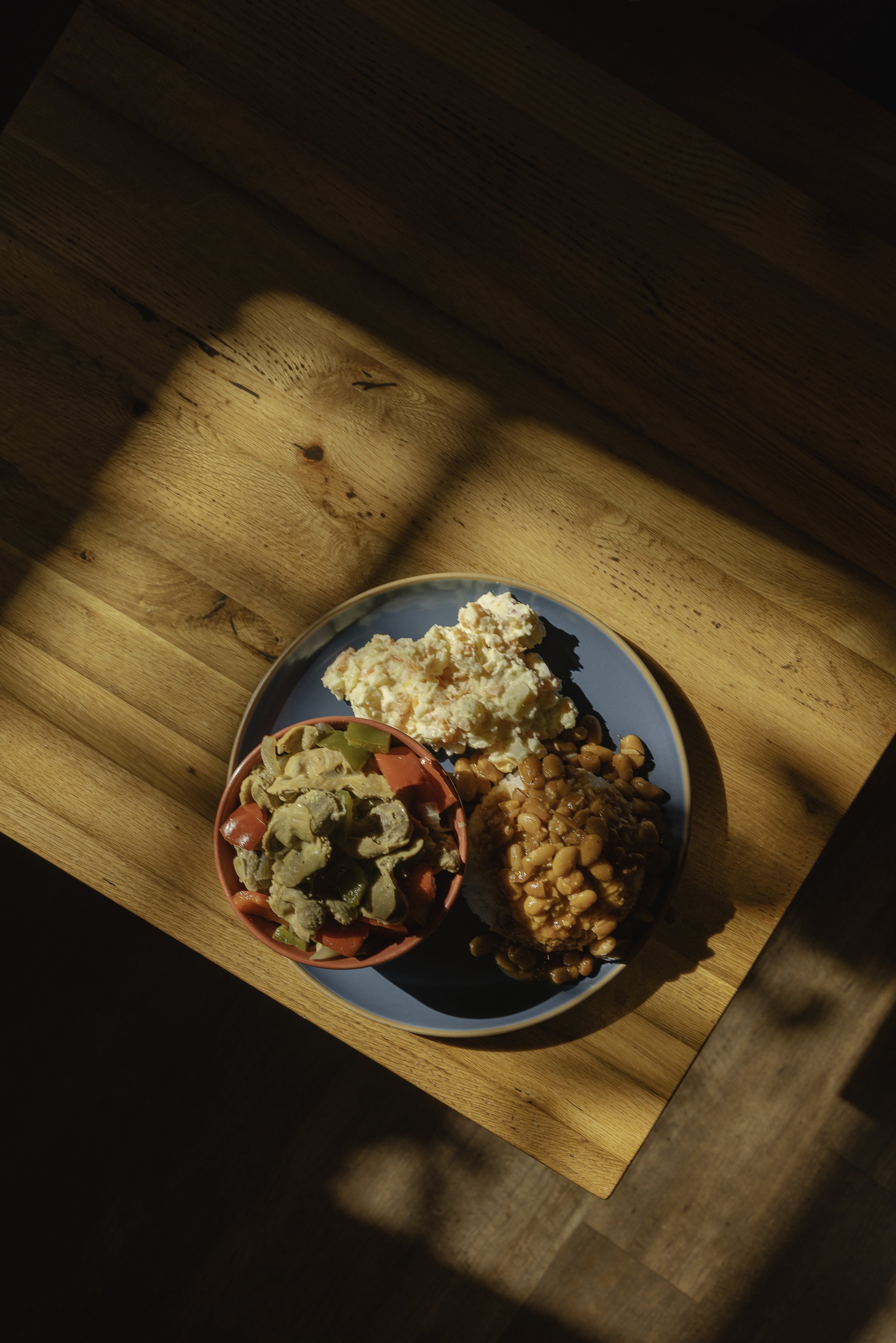 Plate with mashed potatoes, baked beans, and a side salad on a wooden table.