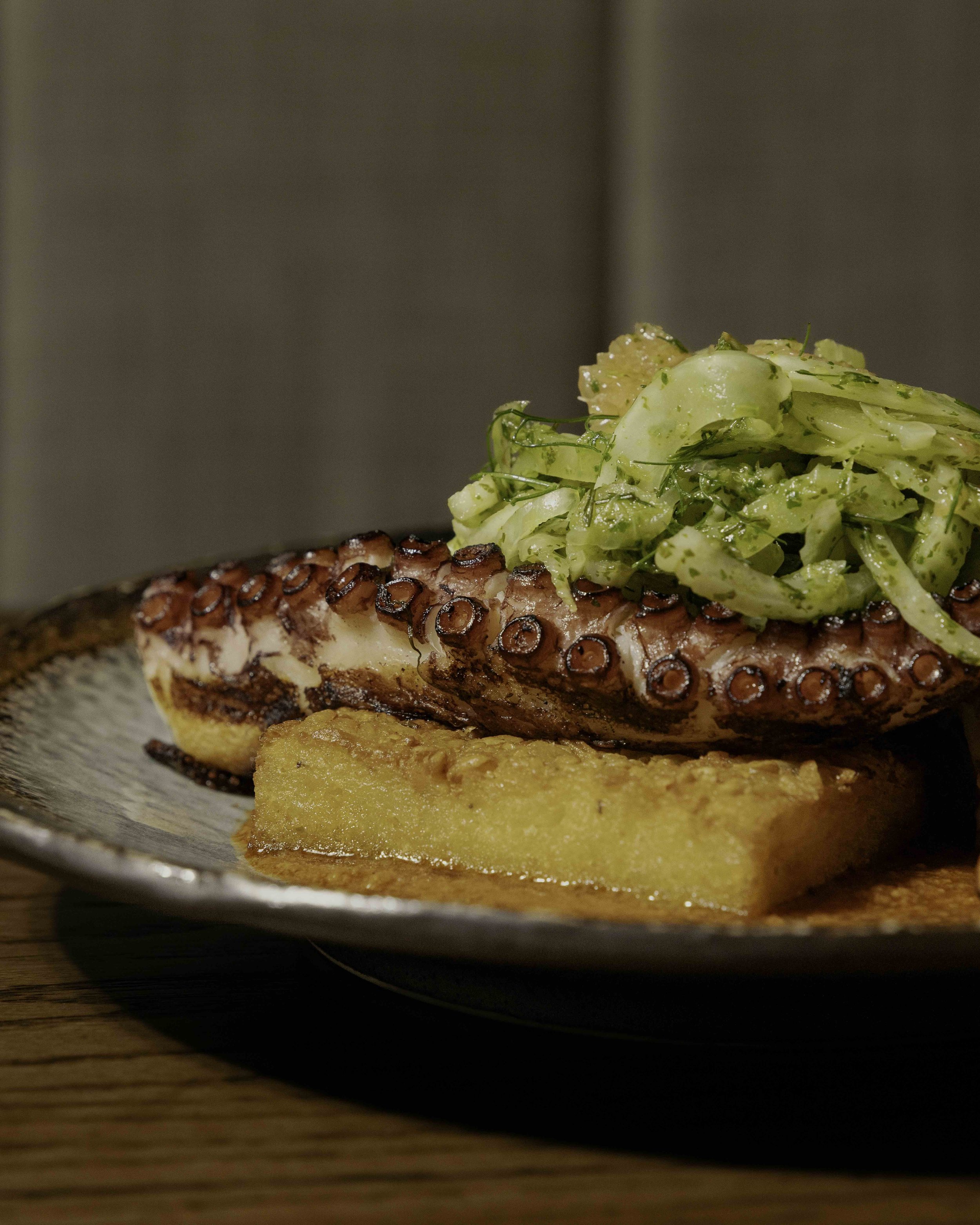 Grilled octopus tentacle served with a side of fried polenta and topped with chopped fennel salad.