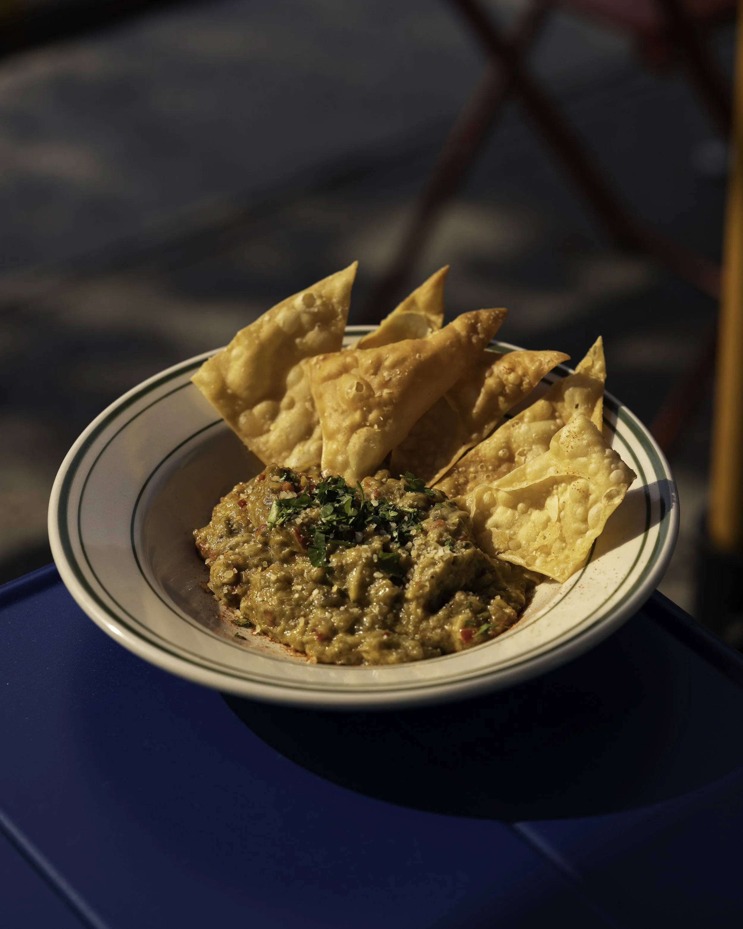 Bowl of Indian food with Samosas and chutney garnished with cilantro, placed on a blue table.