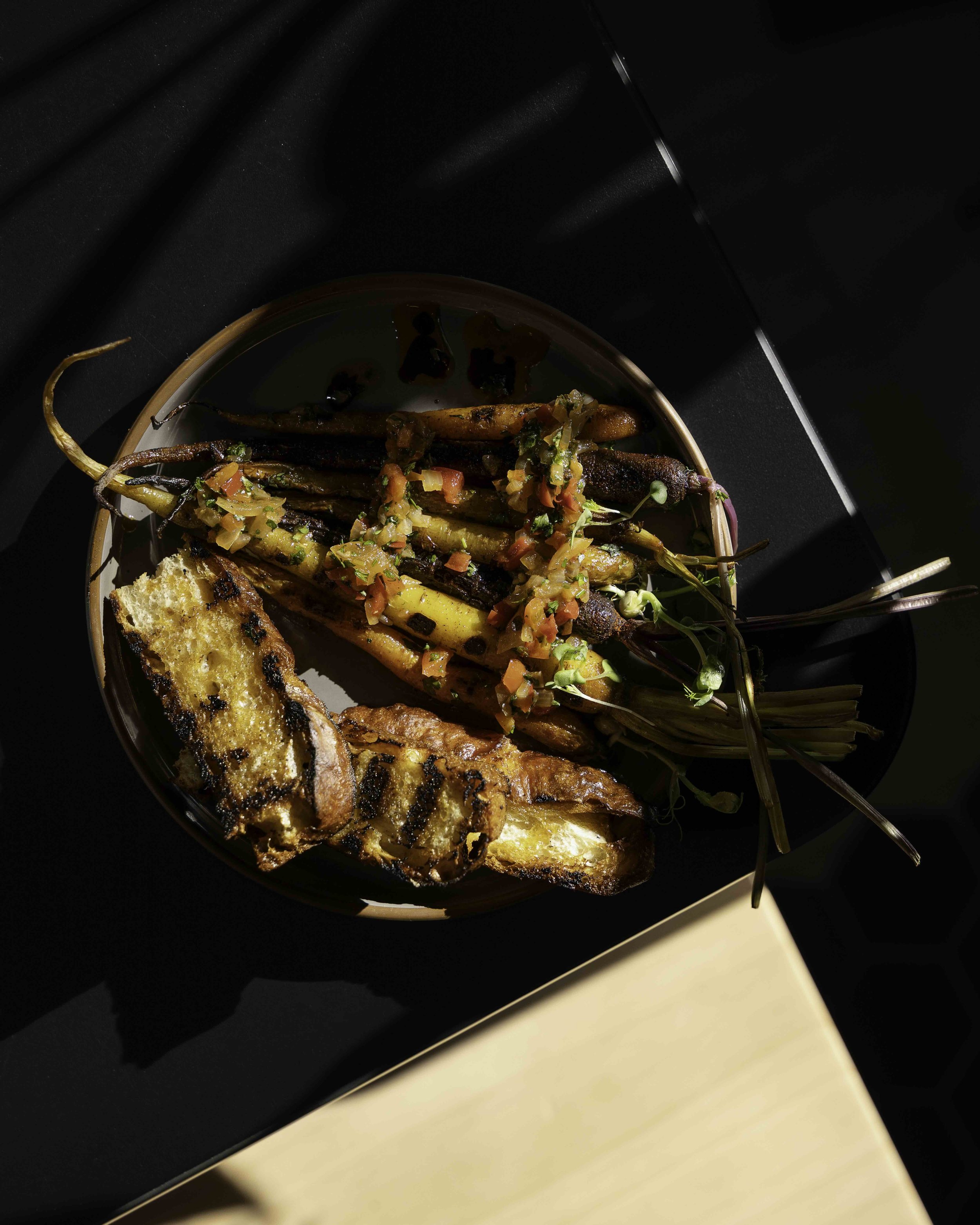 A plate of grilled vegetables, including colorful radish and carrot, topped with salsa, and slices of toasted bread on a dark background.