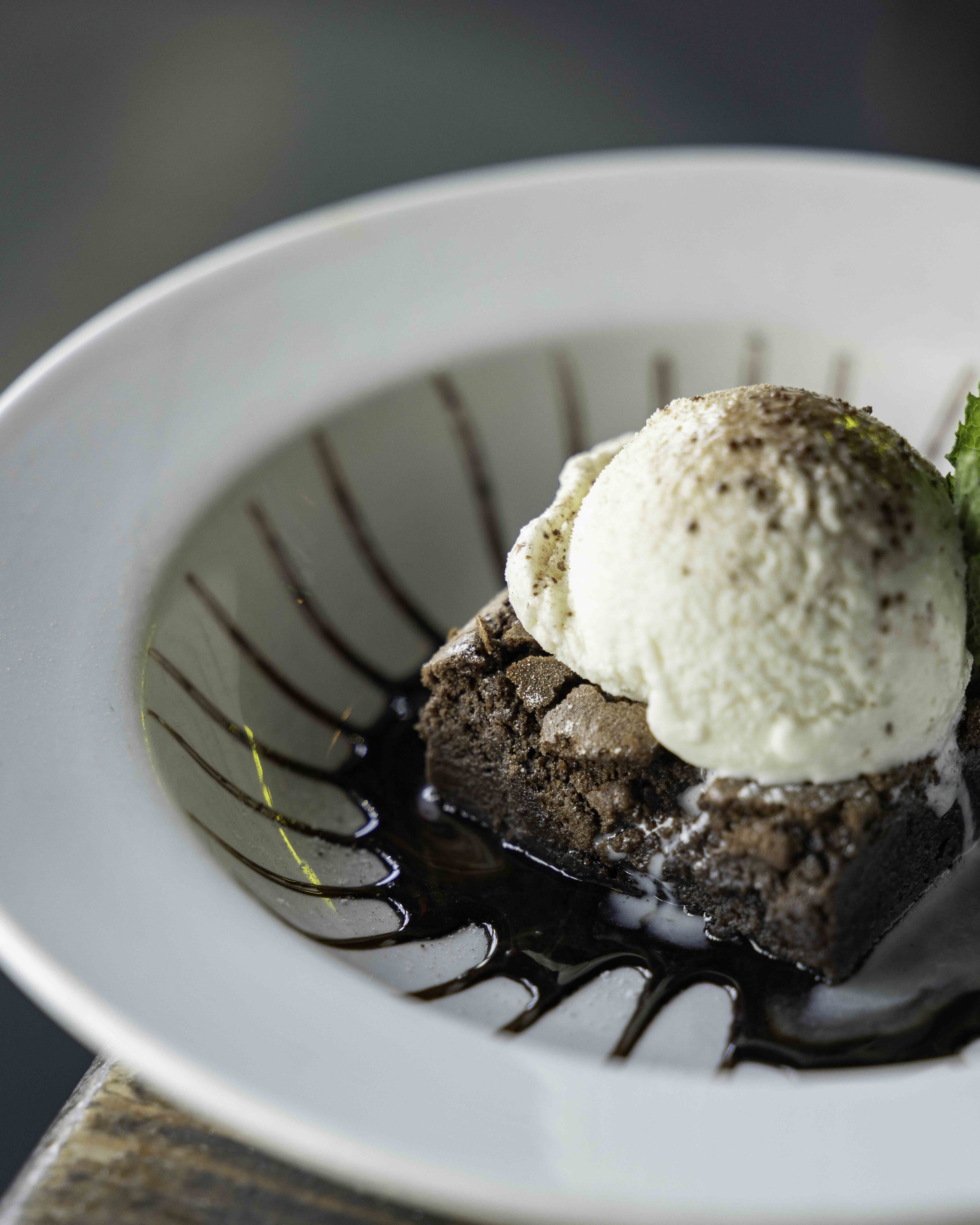 Chocolate brownie with vanilla ice cream, drizzled chocolate sauce, and a mint leaf on a white plate.