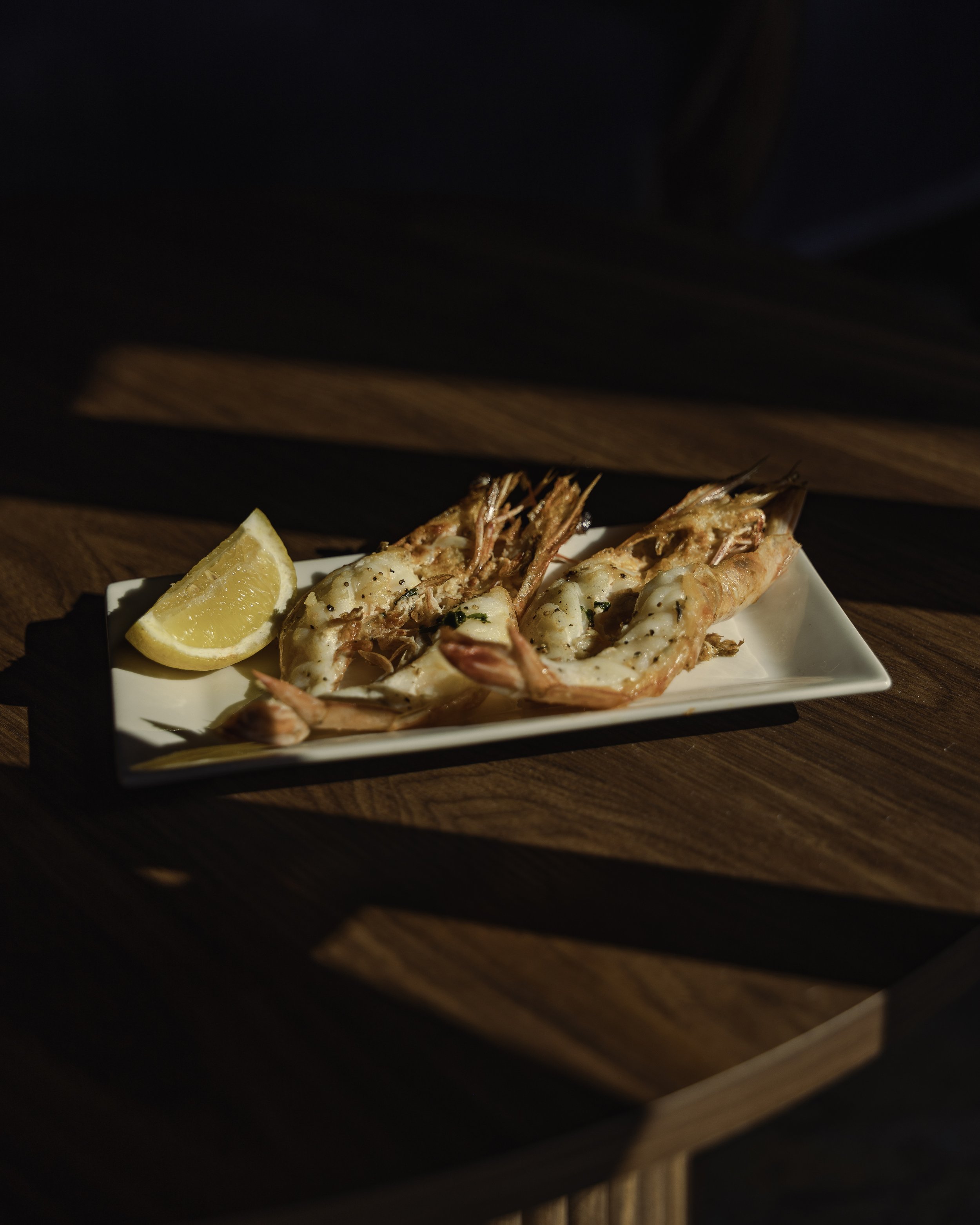Plate of cooked shrimp with lemon wedge on a rectangular white dish on a wooden surface.