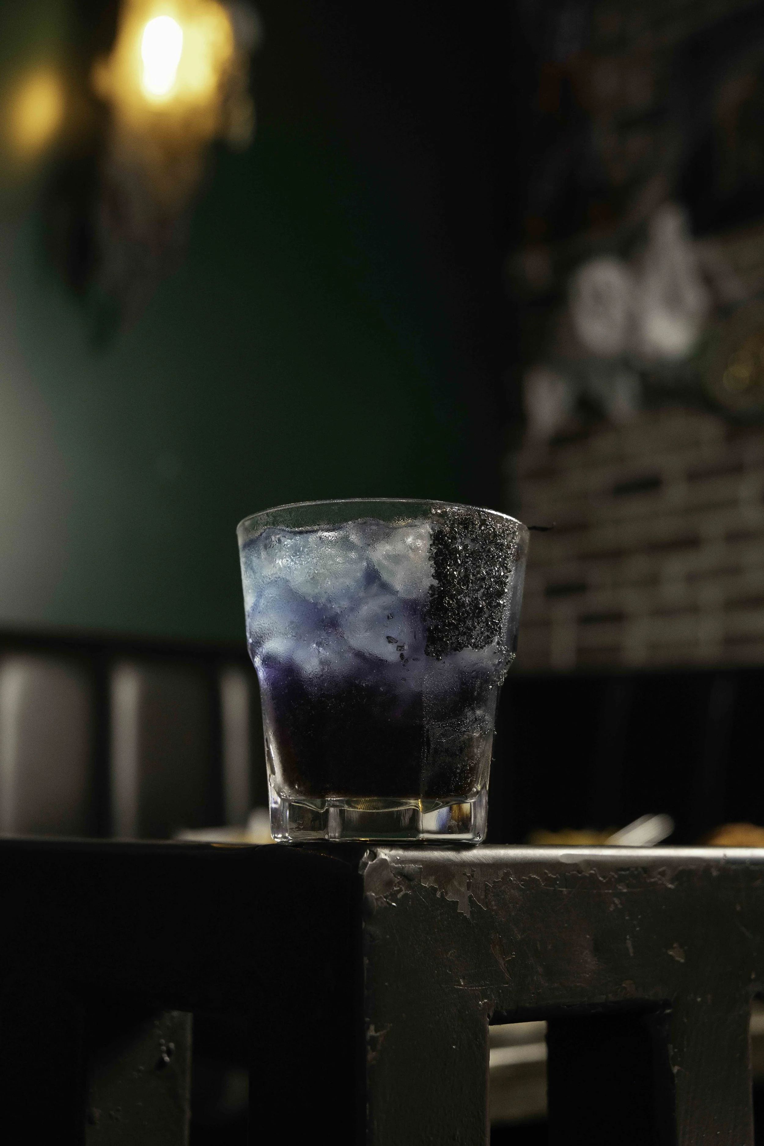 A glass of dark-colored soda with ice cubes on a table in a dimly lit setting, possibly a bar or restaurant.