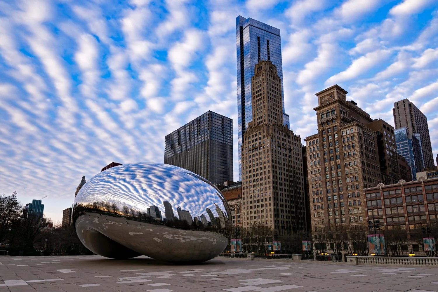 Clouds reflection on the metallic sculpture 'Cloud Gate' in Millennium Park, Chicago, with city skyscrapers in the background.