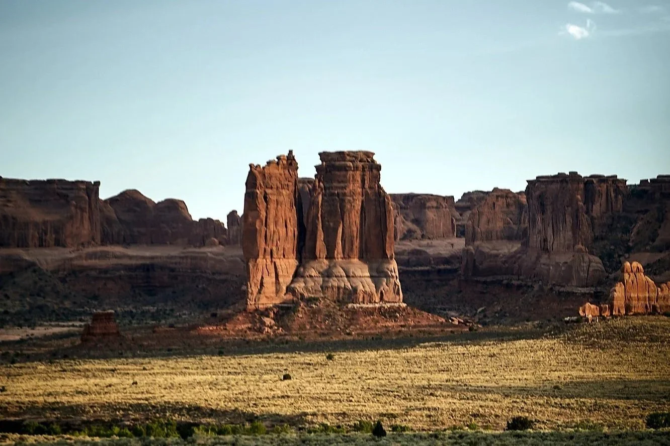 A photo of the landscape at Arches National Park, featuring large red rock formations and a clear blue sky.