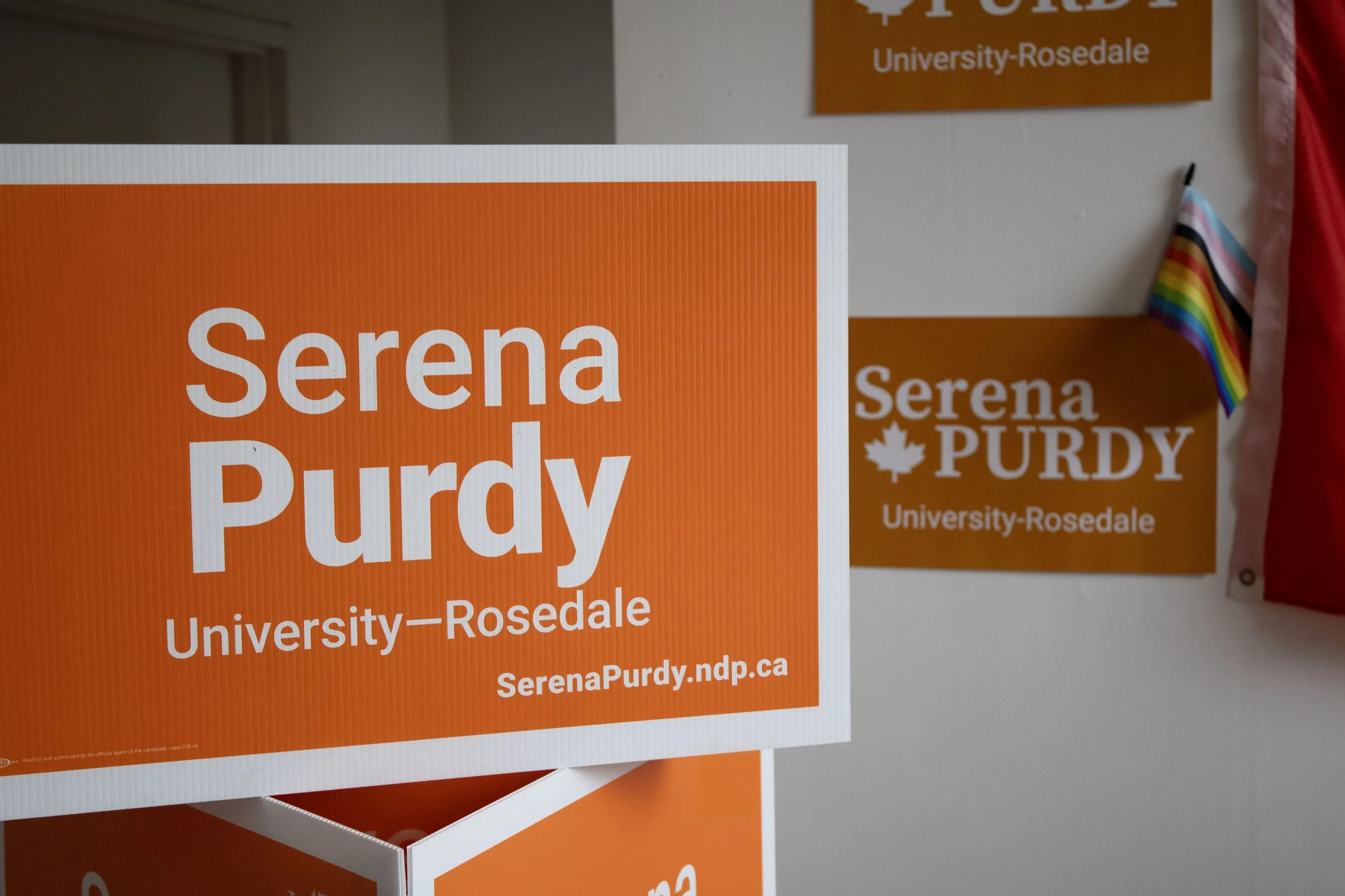 Sign and poster for Serena Purdy, University-Rosedale, with a rainbow flag beside them.