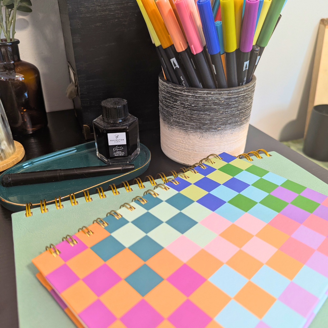 Stack of colorful journals next to a pen holder with color markers