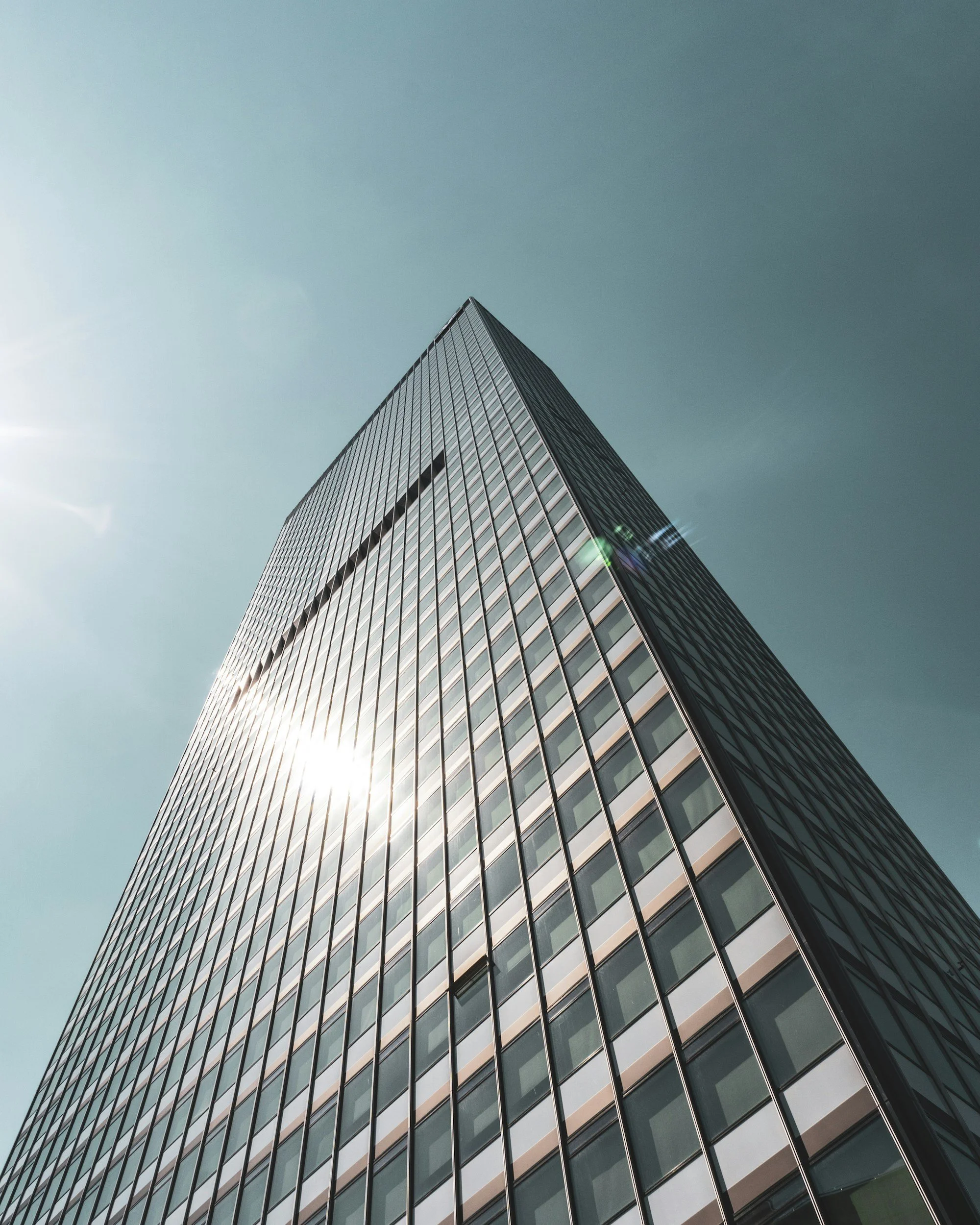 Low-angle view of a modern skyscraper with reflective glass windows against a clear blue sky, sunlight reflecting off the building.