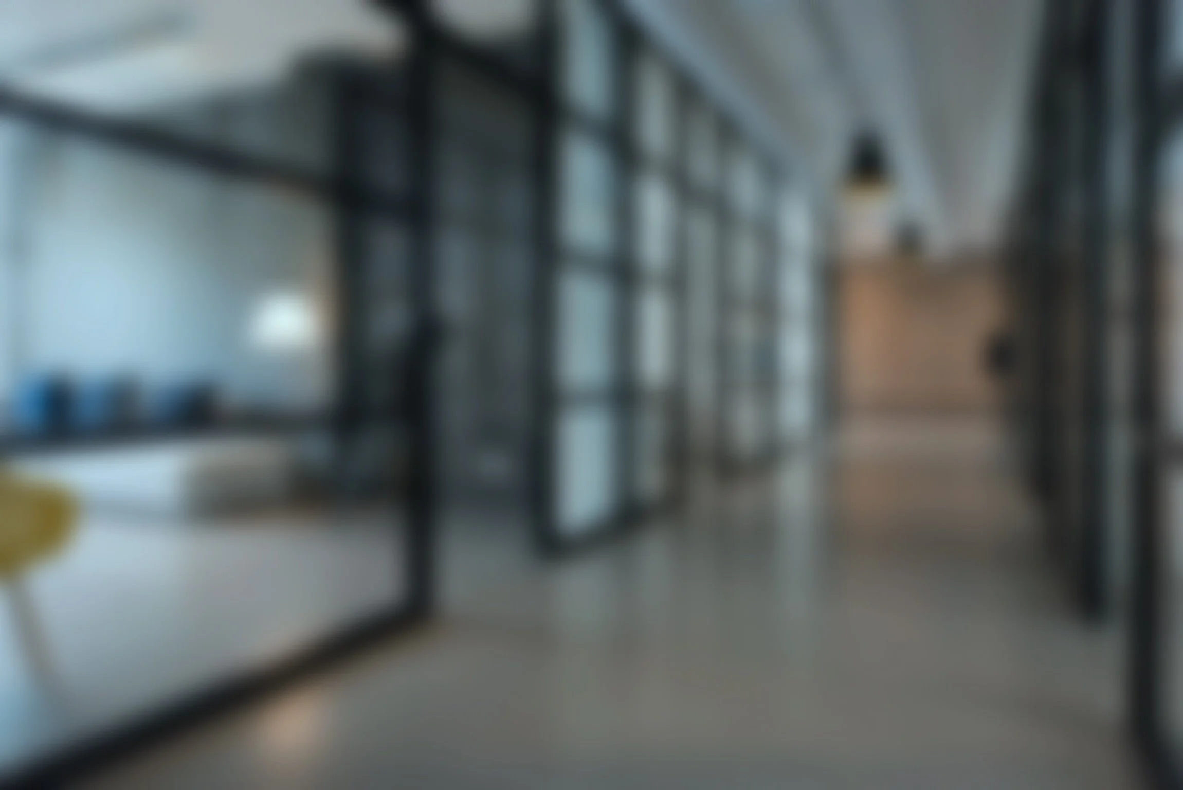 A blurred image of a modern interior space with glass walls and black metal frames, featuring shelving and open doorways.