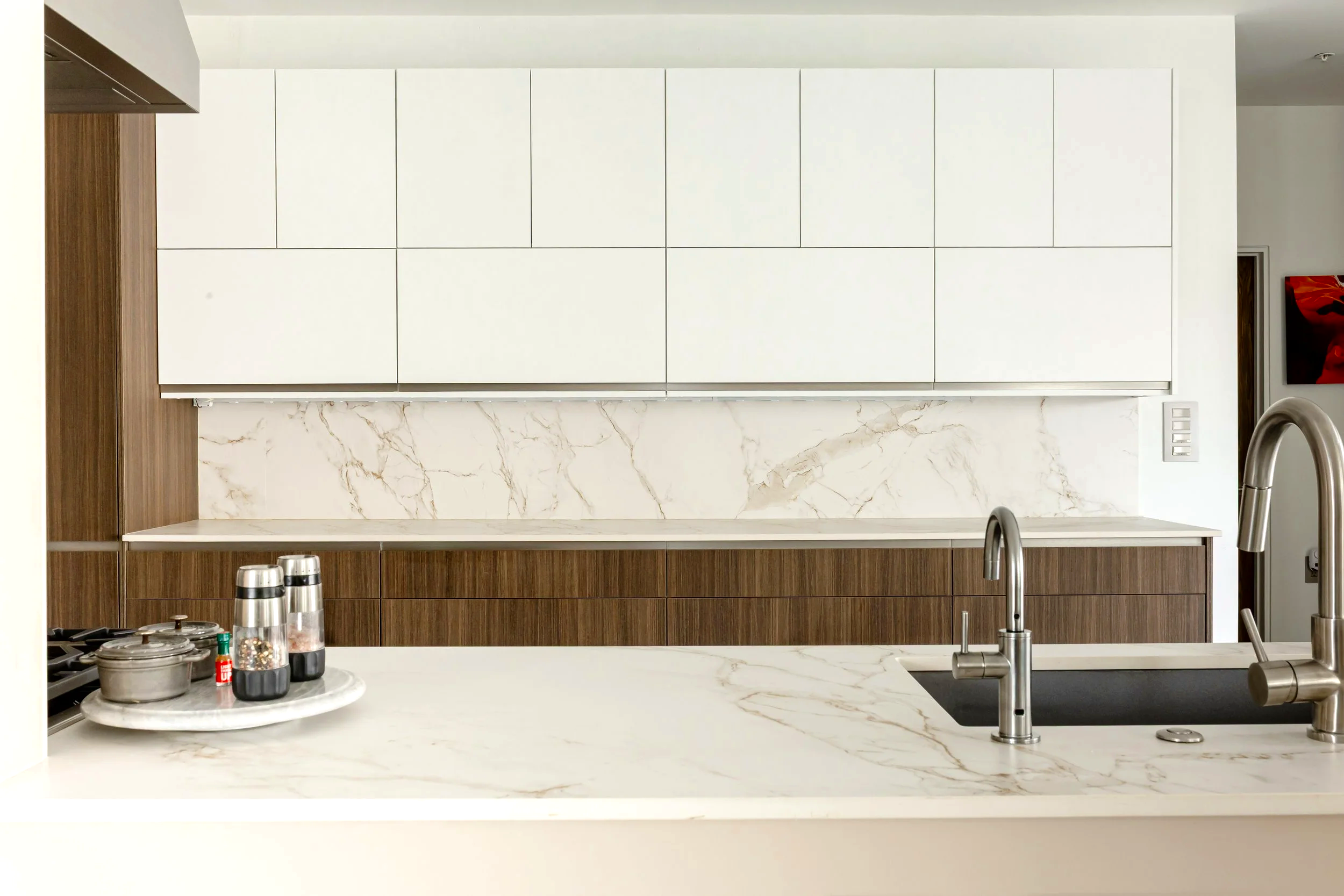 Modern kitchen with white and wood cabinetry, marble backsplash, stone countertop, and stainless steel fixtures.
