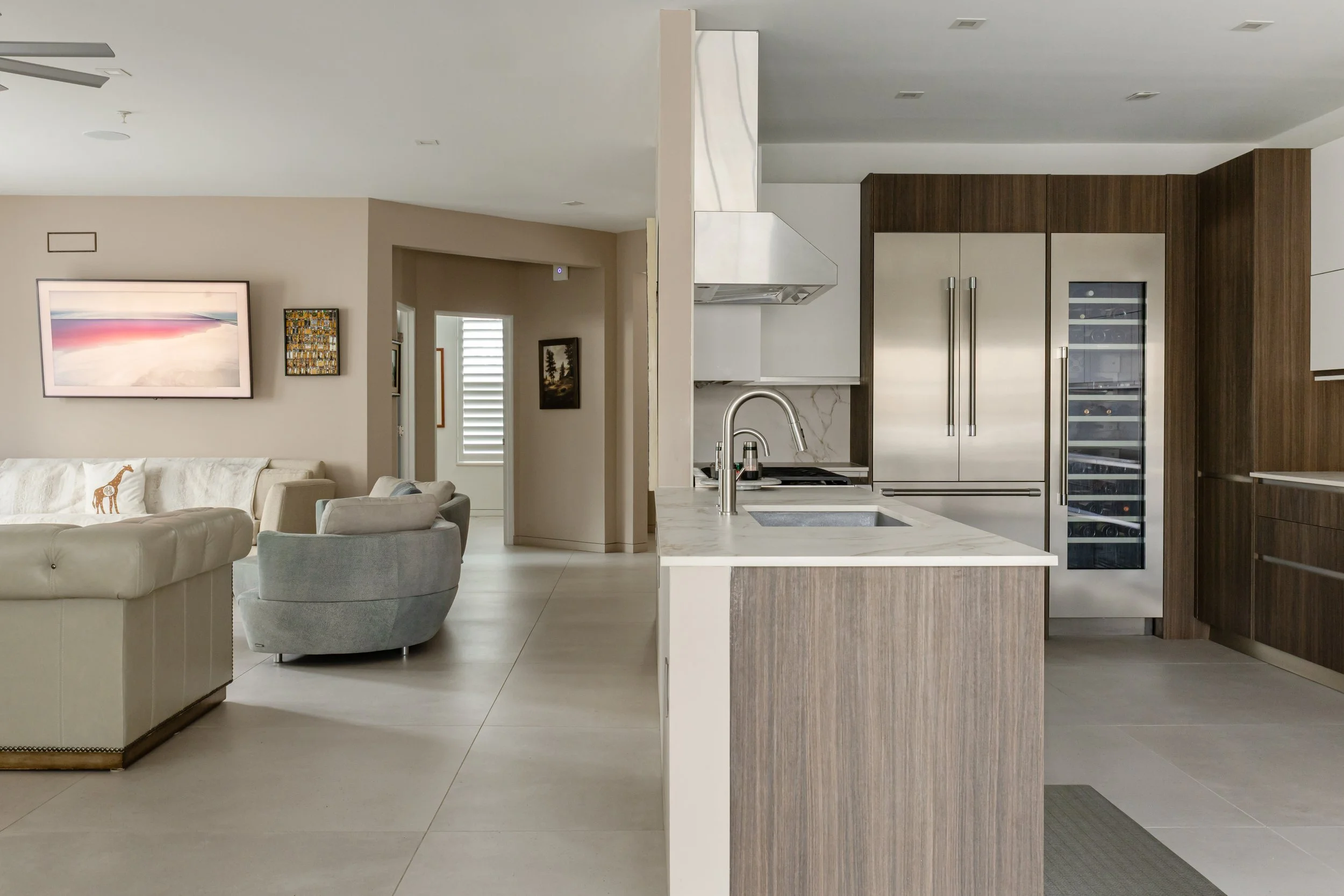 Open-concept living room and modern kitchen with stainless steel appliances, wooden cabinets, marble countertops, and neutral-colored furniture and decor.