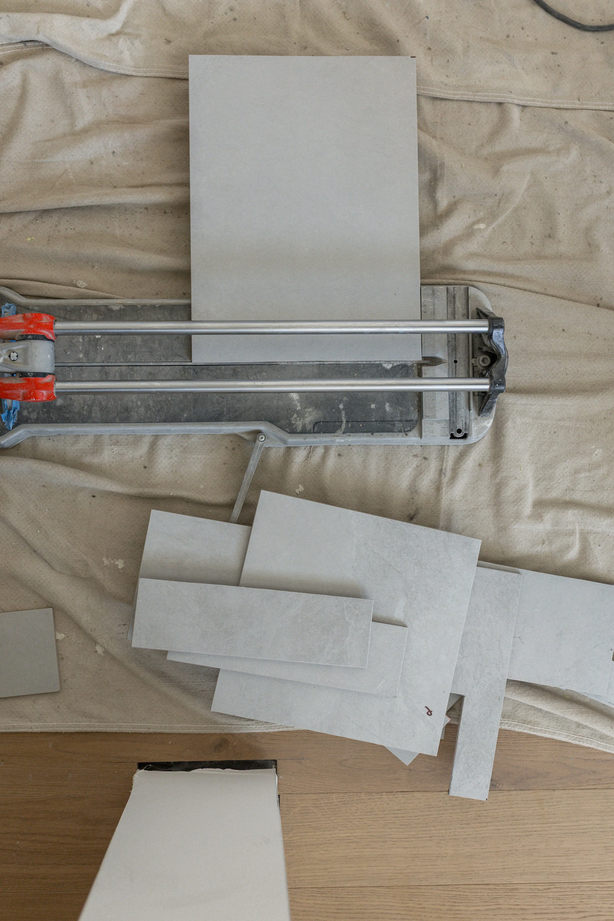 Tile installation tools and tiles on a work surface, including a tile cutter, tiles, and a protective sheet.