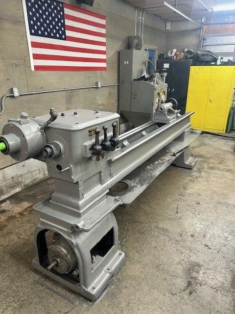 Industrial metal lathe machine in workshop with American flag on wall.