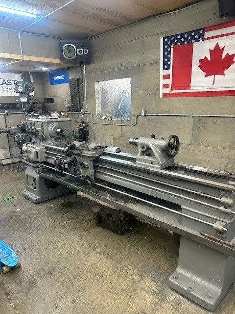 A metal lathe machine in a workshop with an American and Canadian flag hanging on the wall.