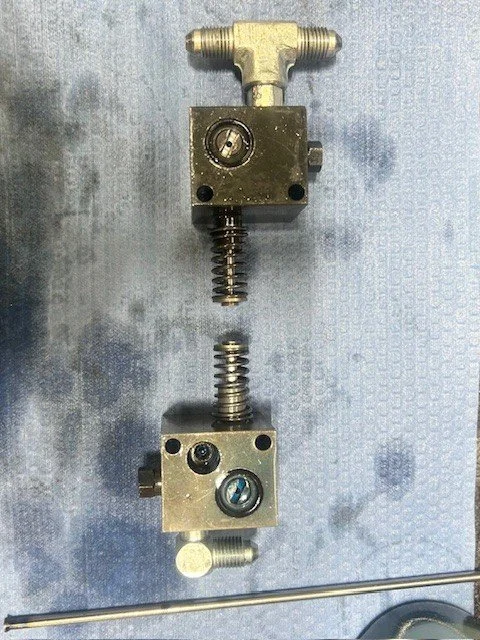 Disassembled hydraulic or pneumatic valve with two blocks connected by springs and fittings.
