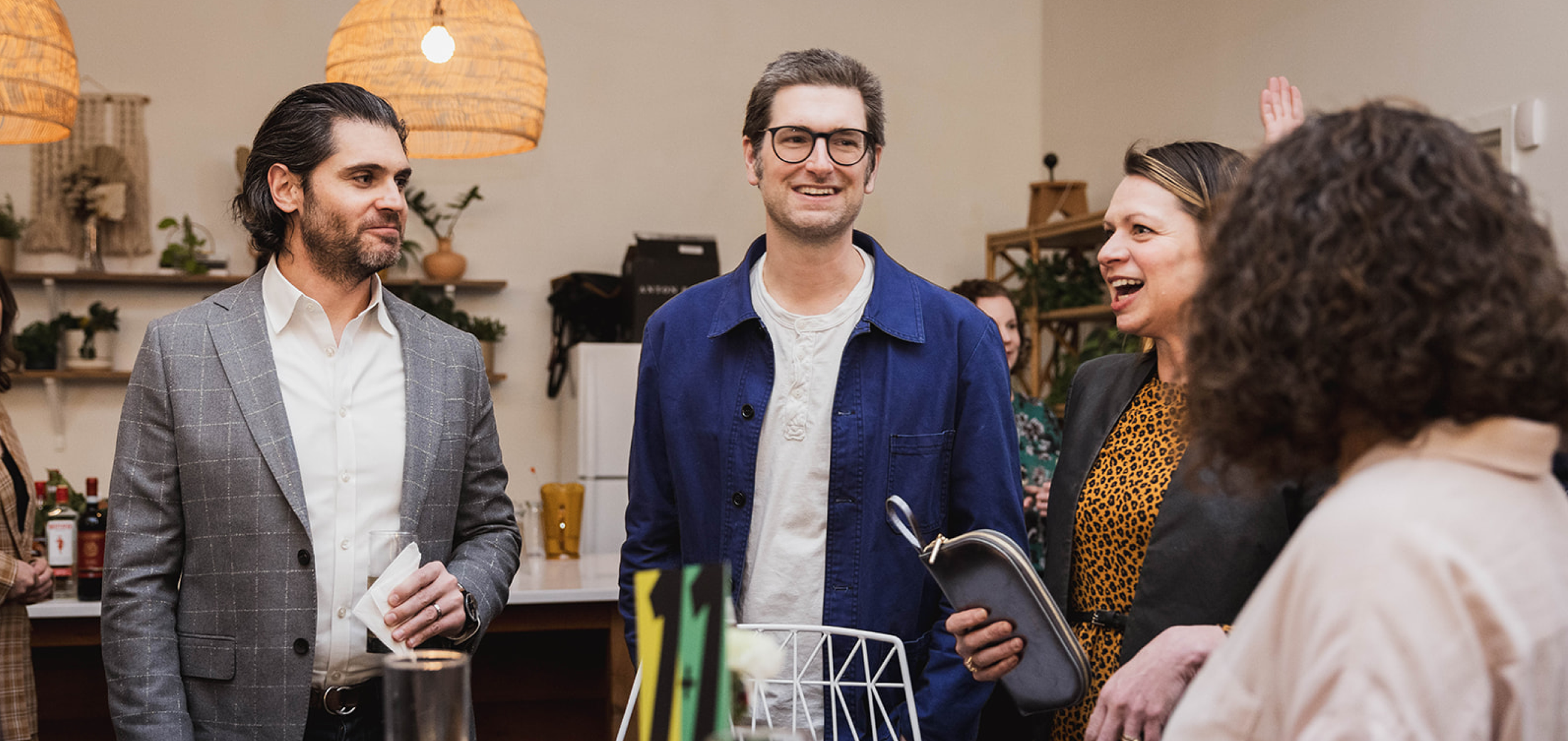 Group of people in a social setting chatting and smiling in a well-lit room, possibly at a gathering or party.