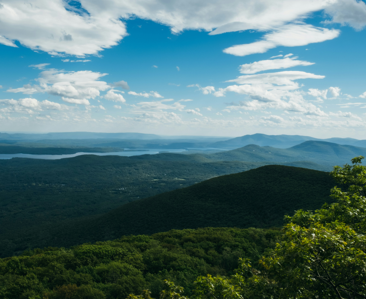 A scenic view of lush green mountains with a blue lake in the distance under a partly cloudy sky.