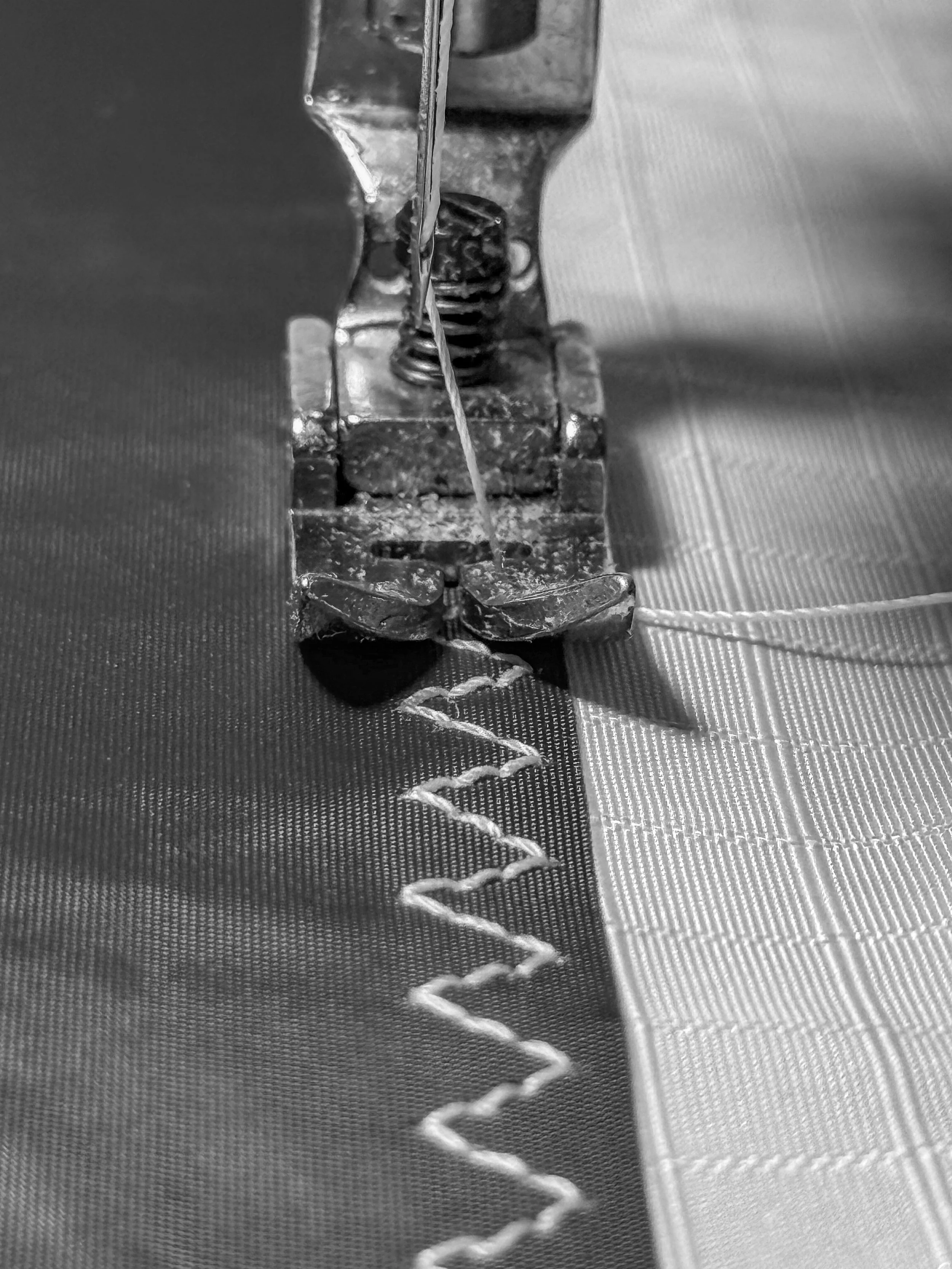 Close-up view of a sewing machine needle stitching fabric, with visible metallic components and thread forming a zigzag pattern.