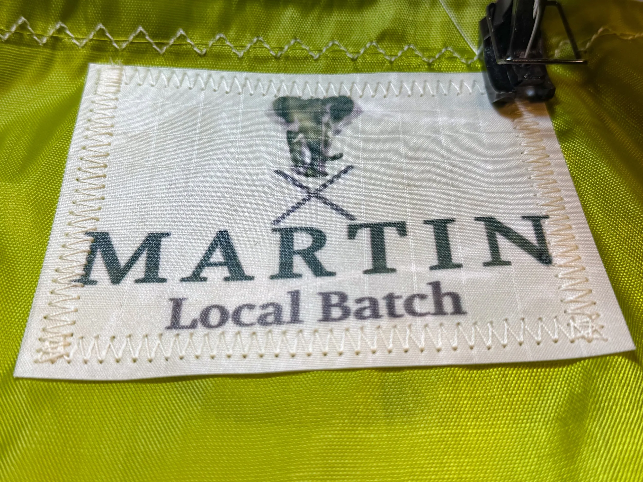 Close-up of a fabric tag with the words 'Maritime Local Batch' and a dog logo, sewn onto yellow-green fabric.
