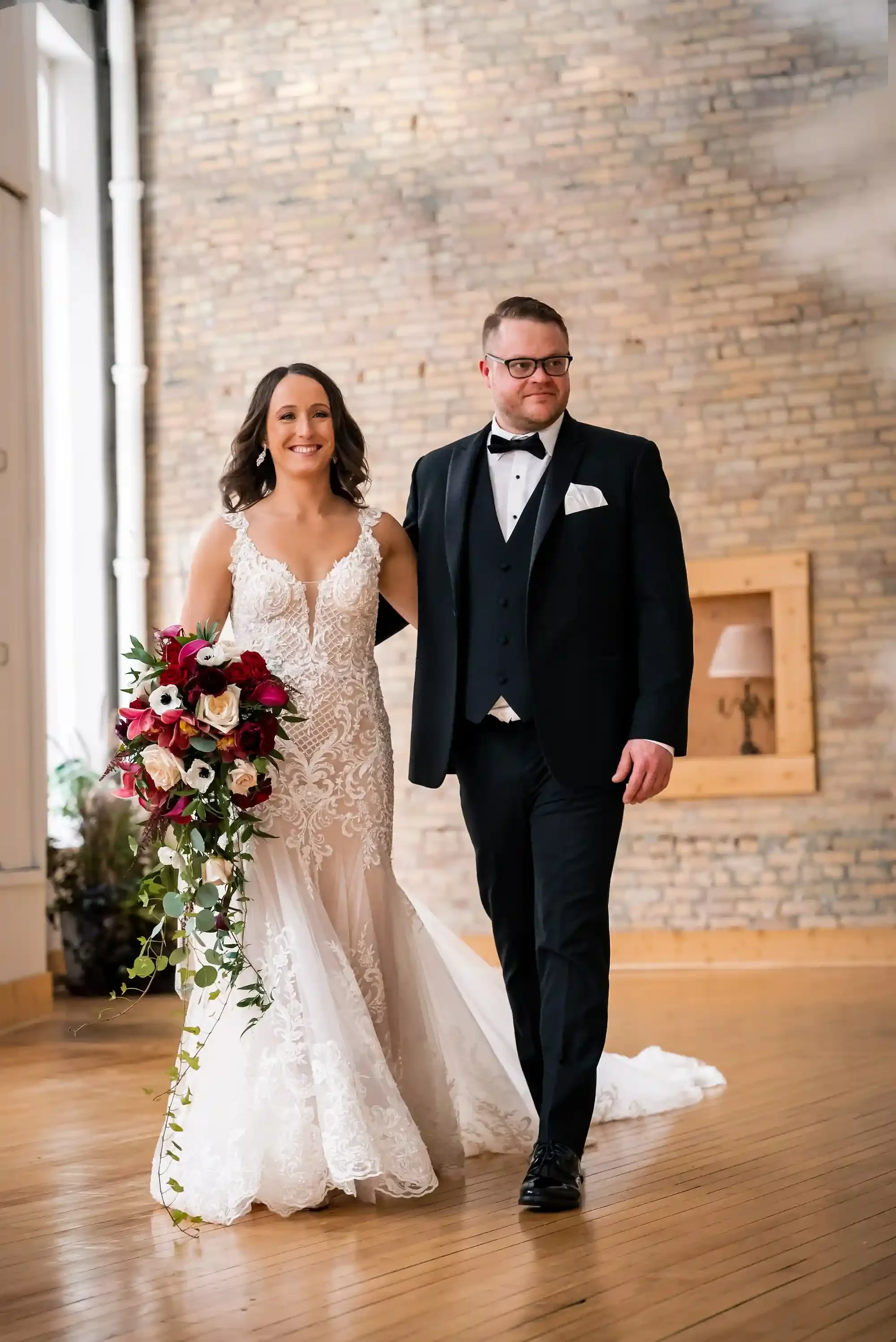 Bride and groom walking through the main event space at The Harlow Exchange wedding venue in Winnipeg's Exchange District, surrounded by exposed brick and hardwood floors