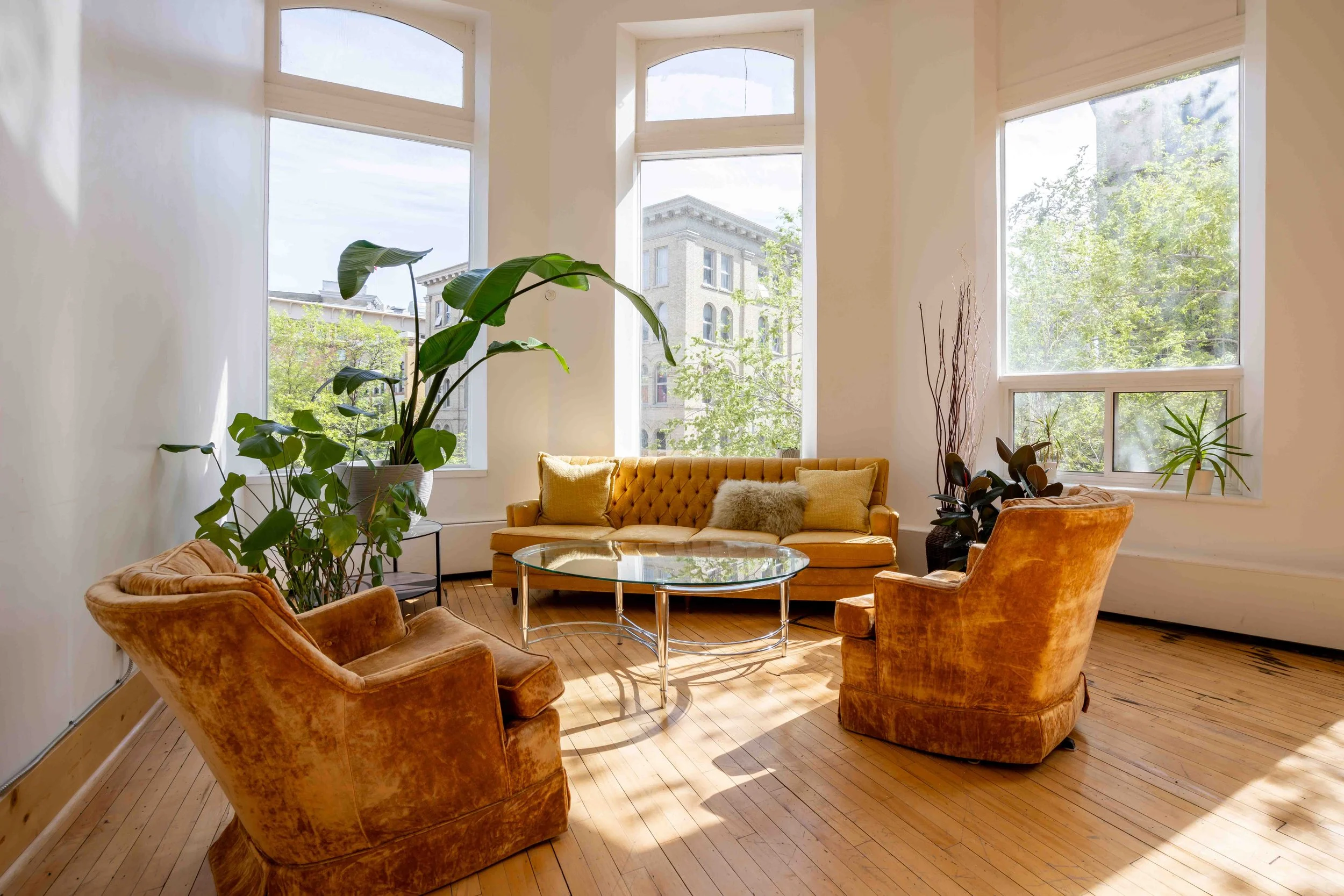 Gold velvet sofa and lounge seating area with floor-to-ceiling windows overlooking Winnipeg's Exchange District at The Harlow Exchange