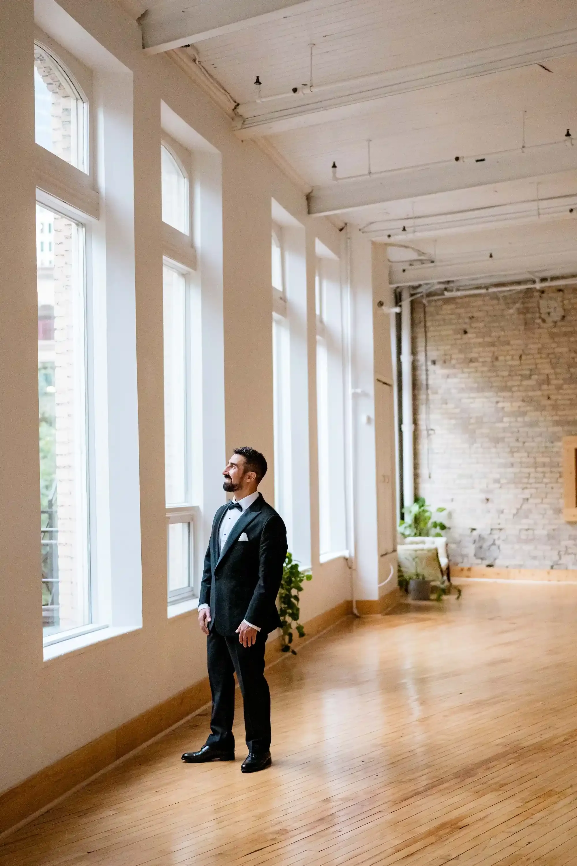 Groom standing at tall windows inside The Harlow Exchange wedding ceremony venue in Winnipeg