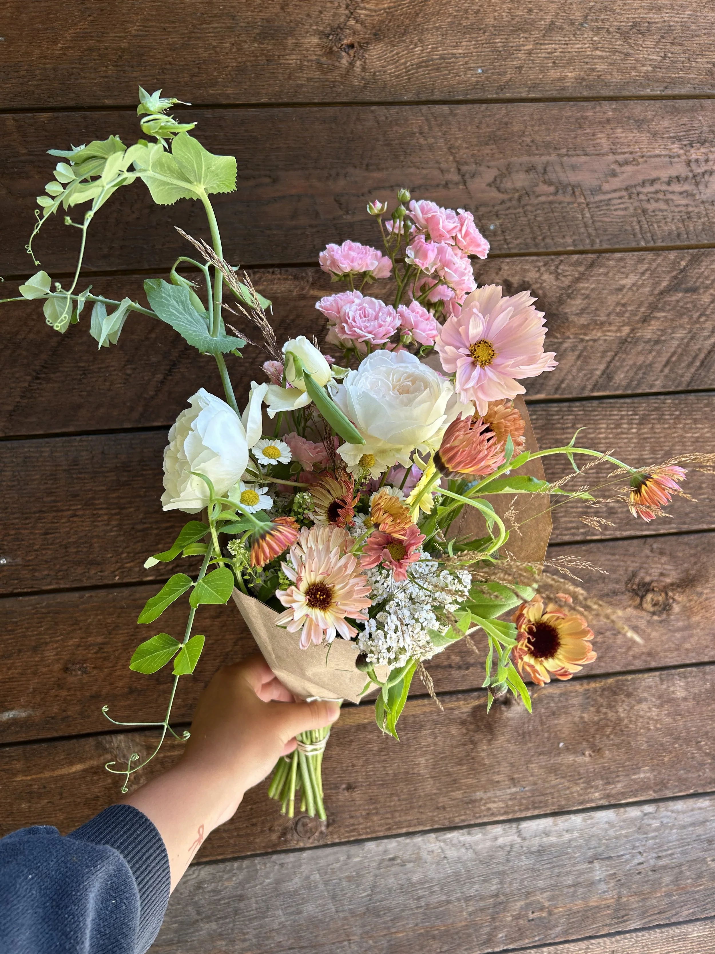 Person holding a bouquet of mixed pink, white, and orange flowers against a wooden background.